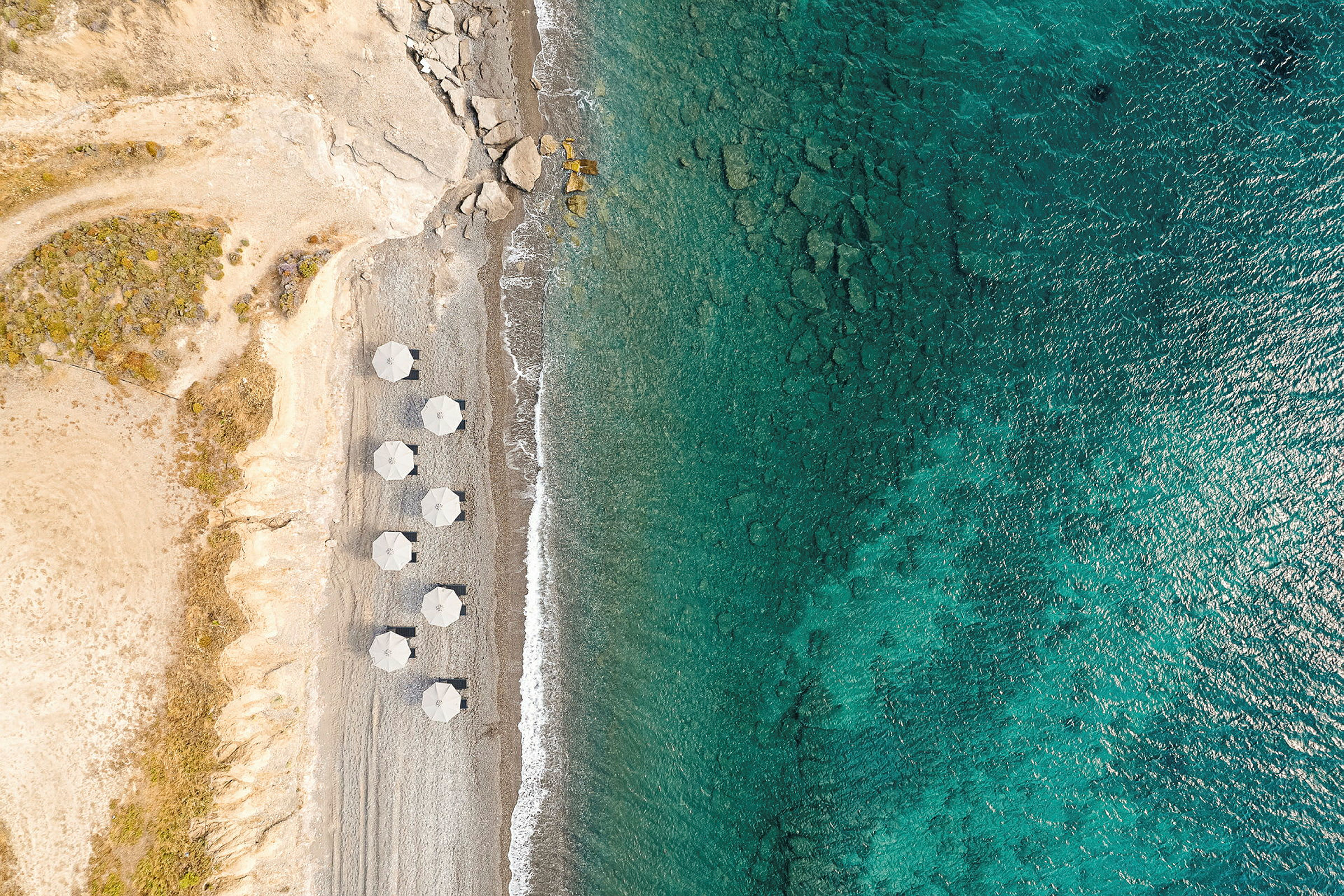 Luftfoto av en strand med parasoller og klart blått hav. (AI-generert tekst)