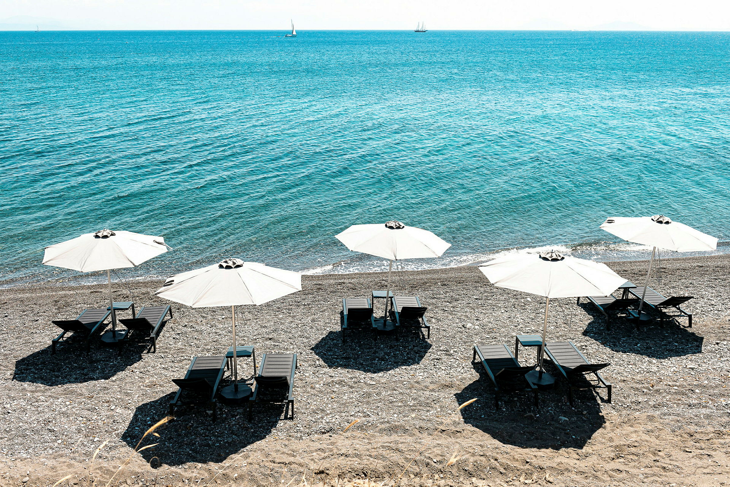 Strand med solsenger under hvite parasoller ved havet. (AI-generert tekst)