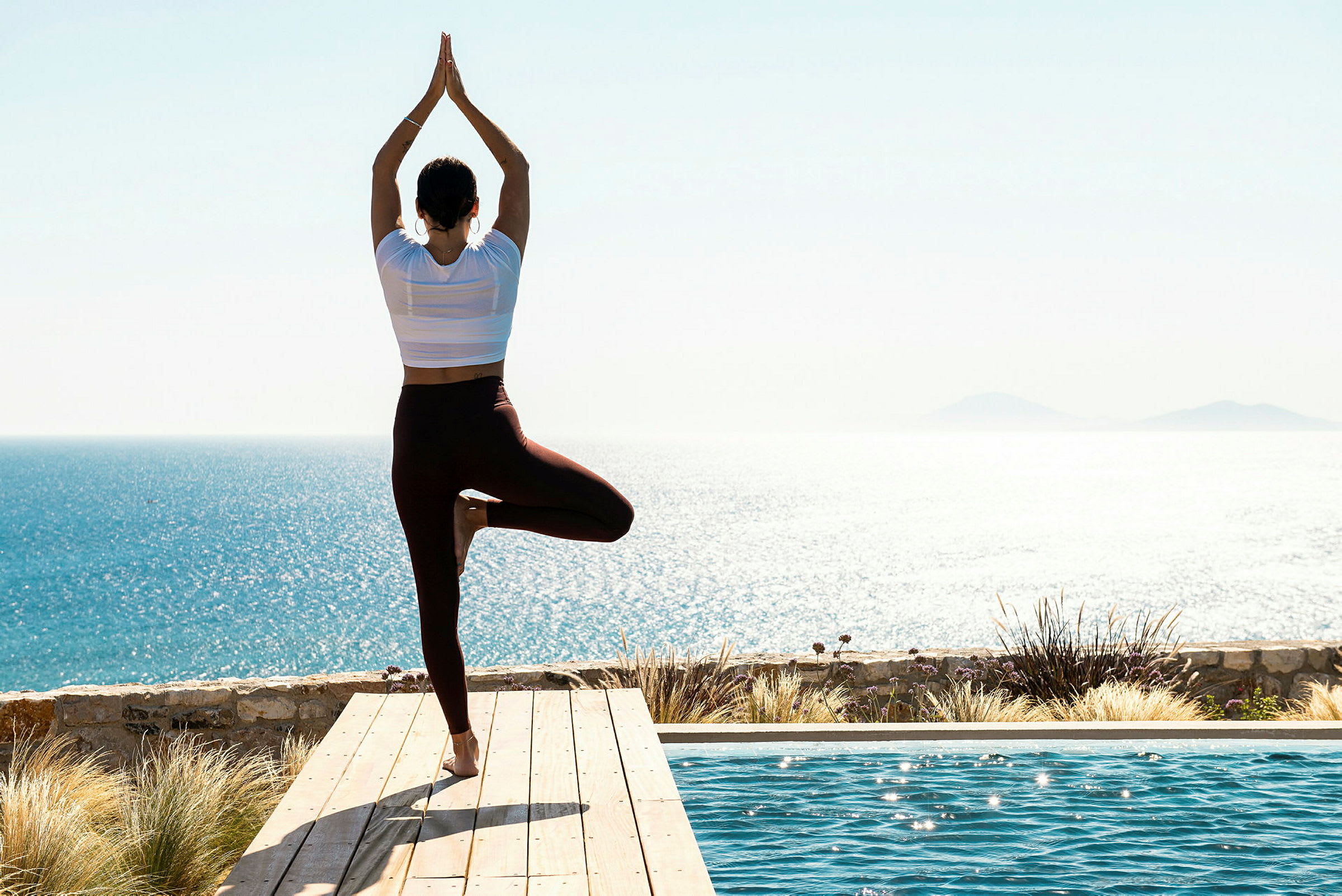 Person som utfører yoga ved et svømmebasseng med havutsikt. (AI-generert tekst)