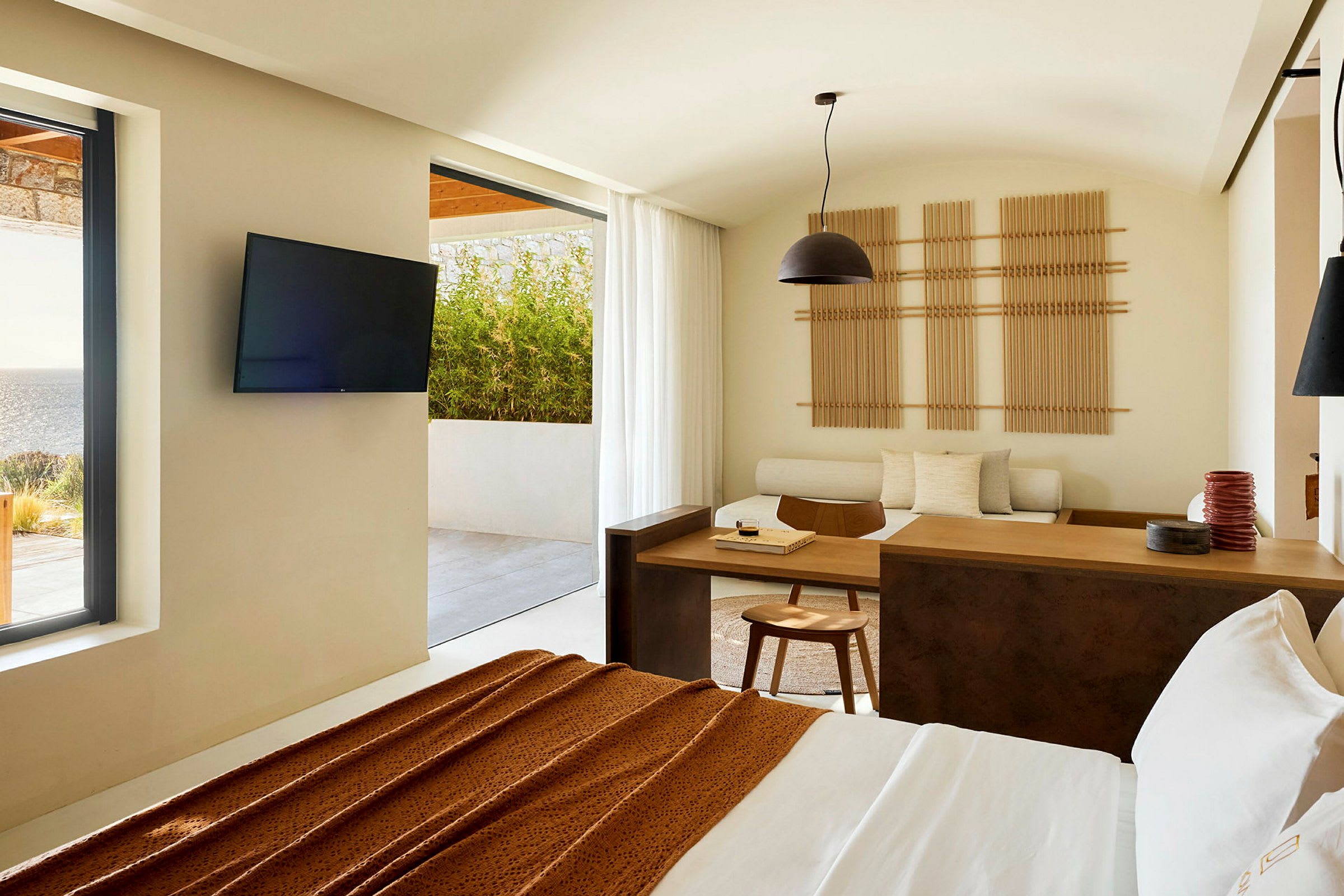 Et moderne hotellrom med utsikt mot en terrasse og havet, innredet med minimalistiske møbler og lyse farger. (AI-generert tekst)