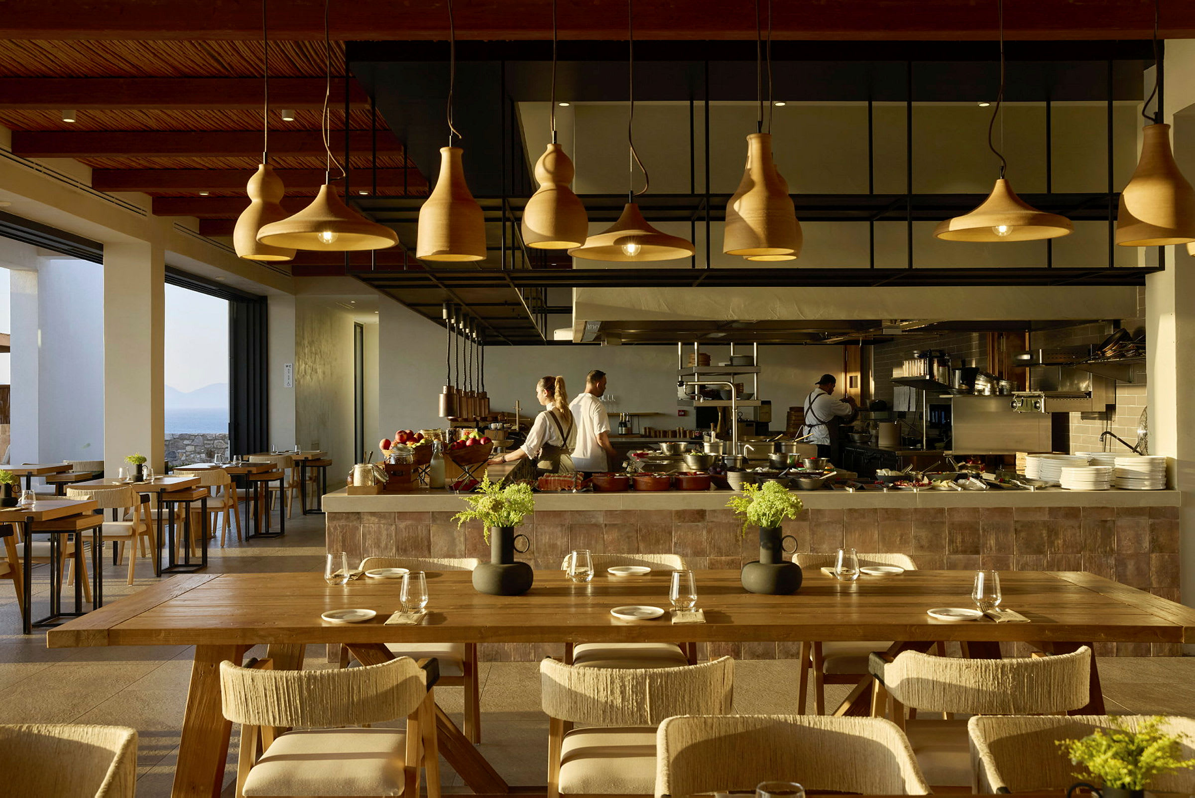 En moderne restaurantmiljø med elegante tre- og lysdesigndetaljer, hvor kokker arbeider bak en serveringsdisk. (AI-generert tekst)