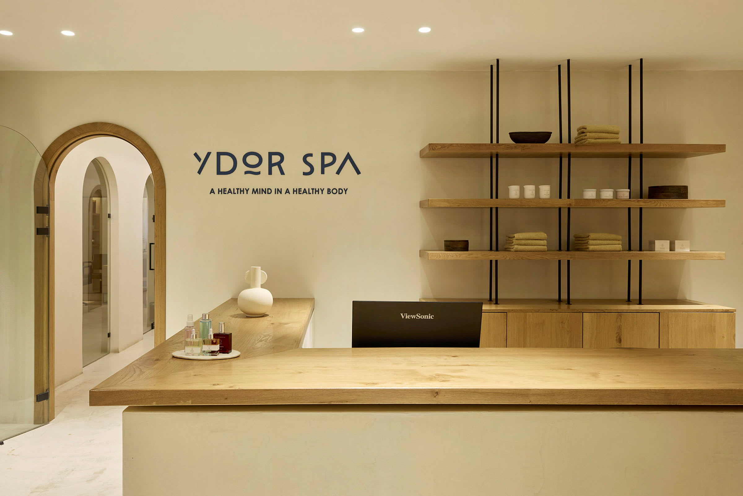 En resepsjonsdisk i et spa med produkter og håndklær på hyller bak. (AI-generert tekst)