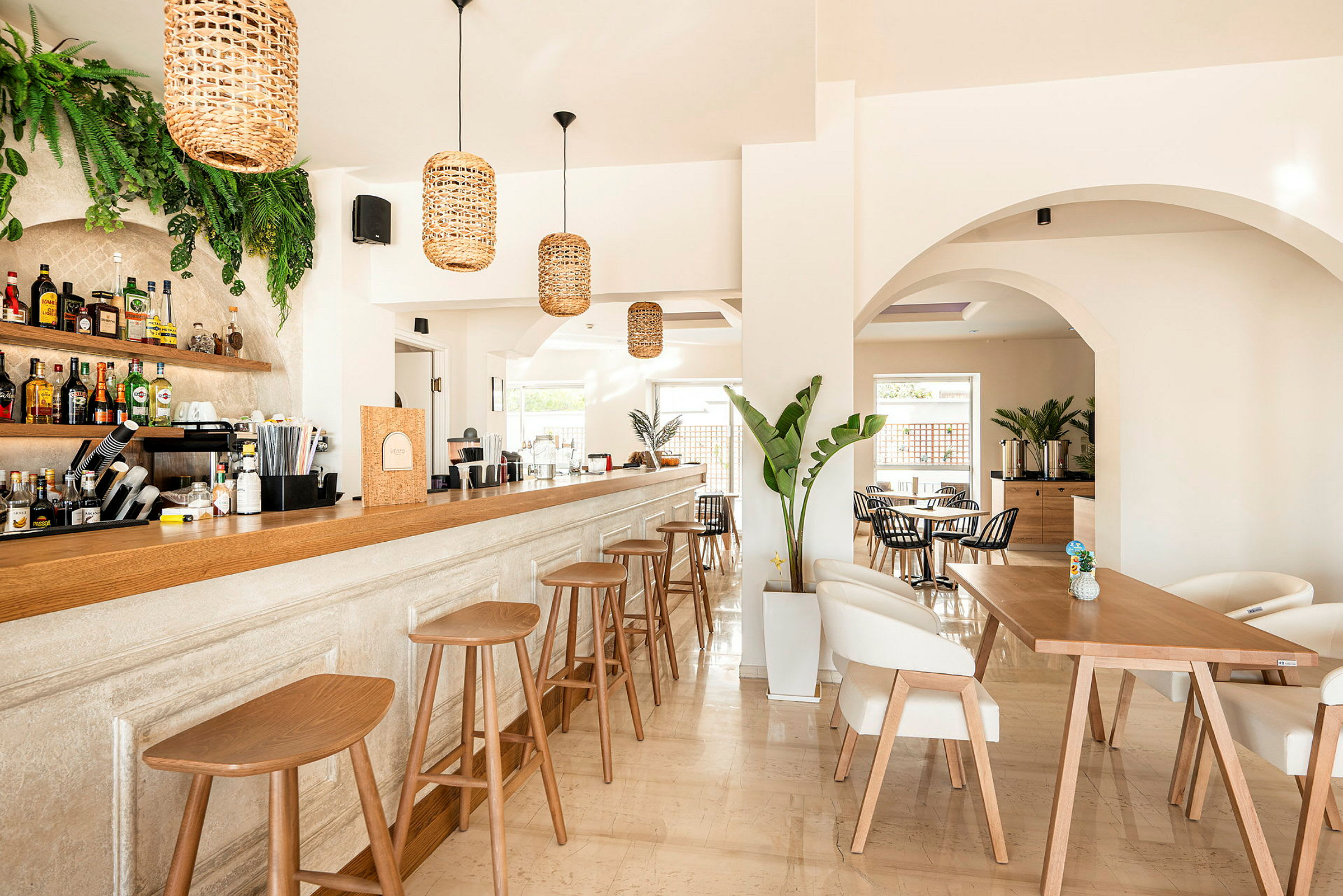 En elegant innredet bar med moderne trestoler og en lang bardisk, omgitt av lyse vegger og plantepynt. (AI-generert tekst)