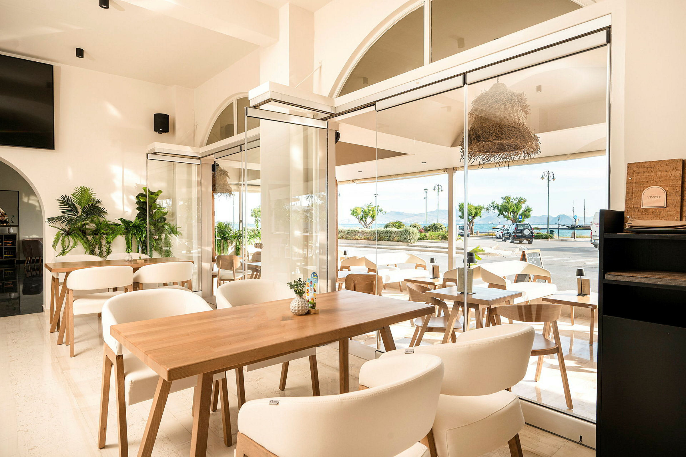 En lys og moderne innredet kafé med store vinduer vendt mot en gate og havutsikt. (AI-generert tekst)