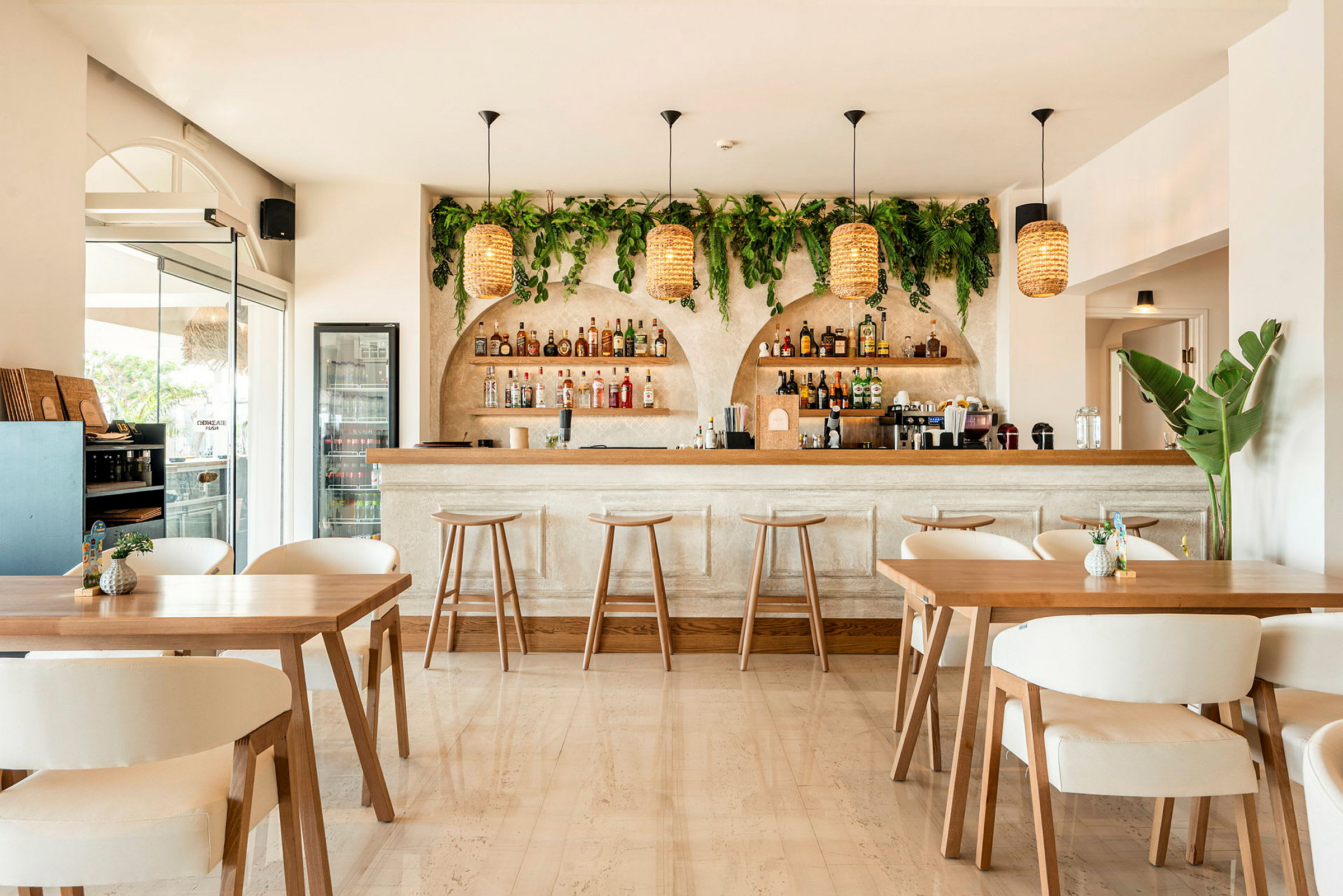 Bilde av en stilren bar med lys innredning. Baren har omsluttende grønn plantepynt samt hengende flettede lamper. (AI-generert tekst)
