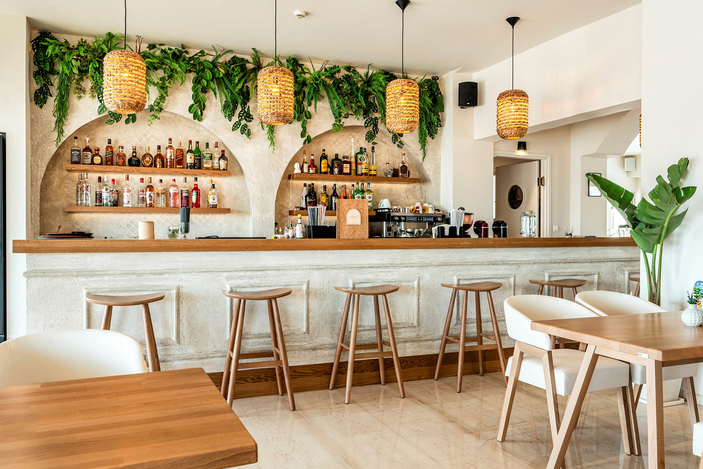 Et interiørbilde av en moderne bar med trestoler, bord og grønne planter på veggene. (AI-generert tekst)