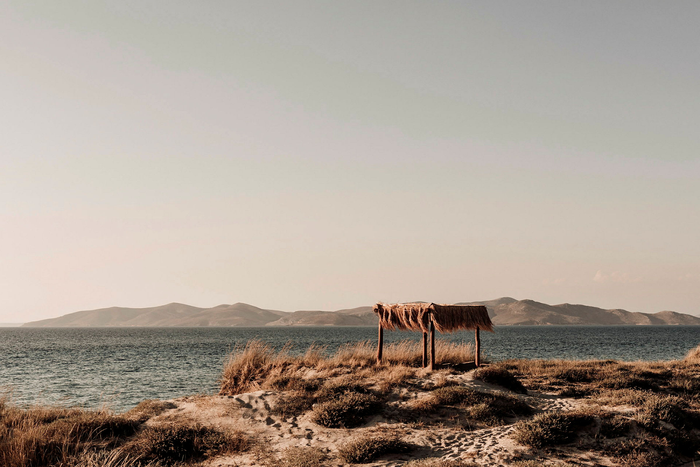 Et strandlandskap med et enkelt skjul av tre og halm ved havet. (AI-generert tekst)