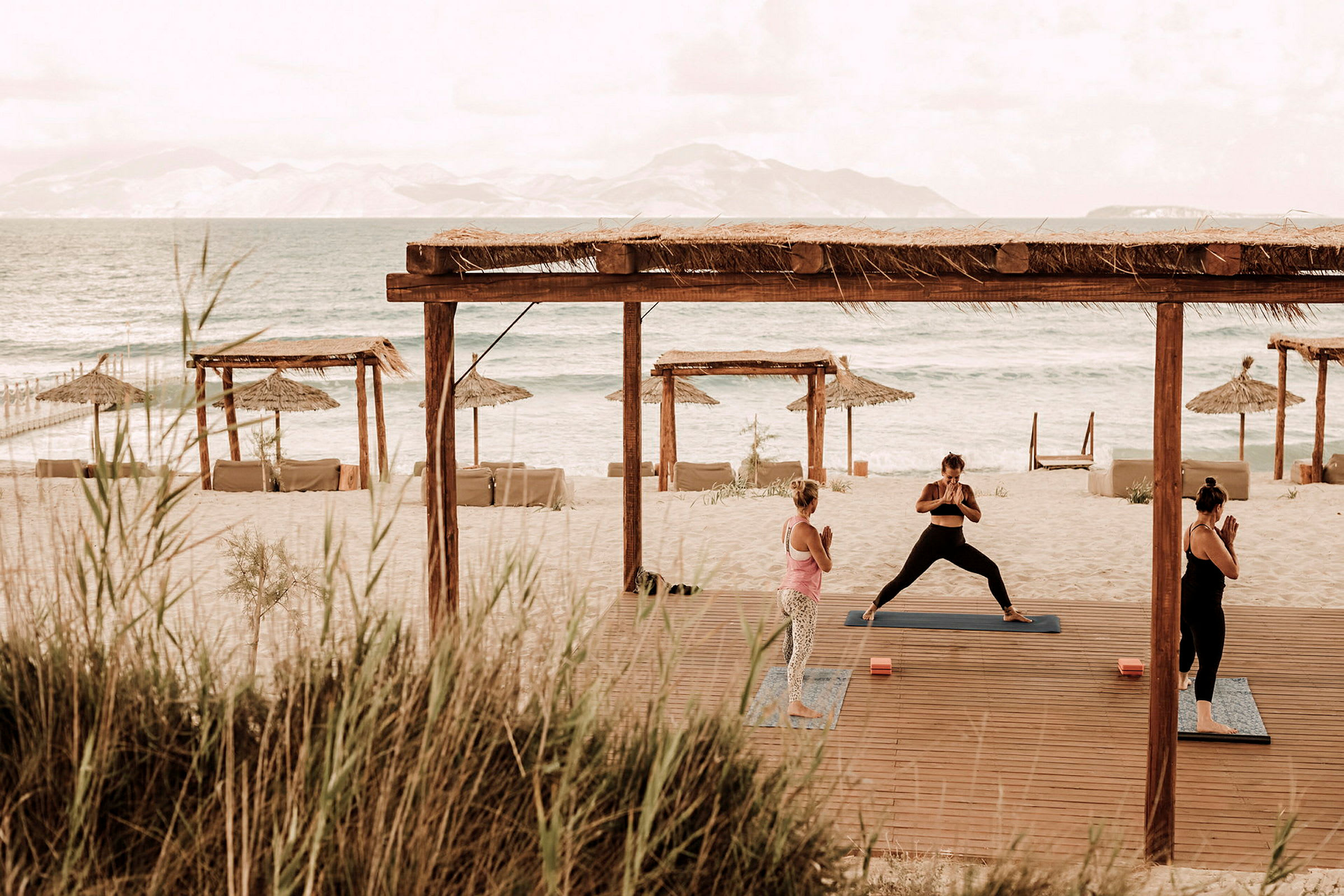 Personer utfører yoga på en strand med utsikt over havet og parasoller. (AI-generert tekst)