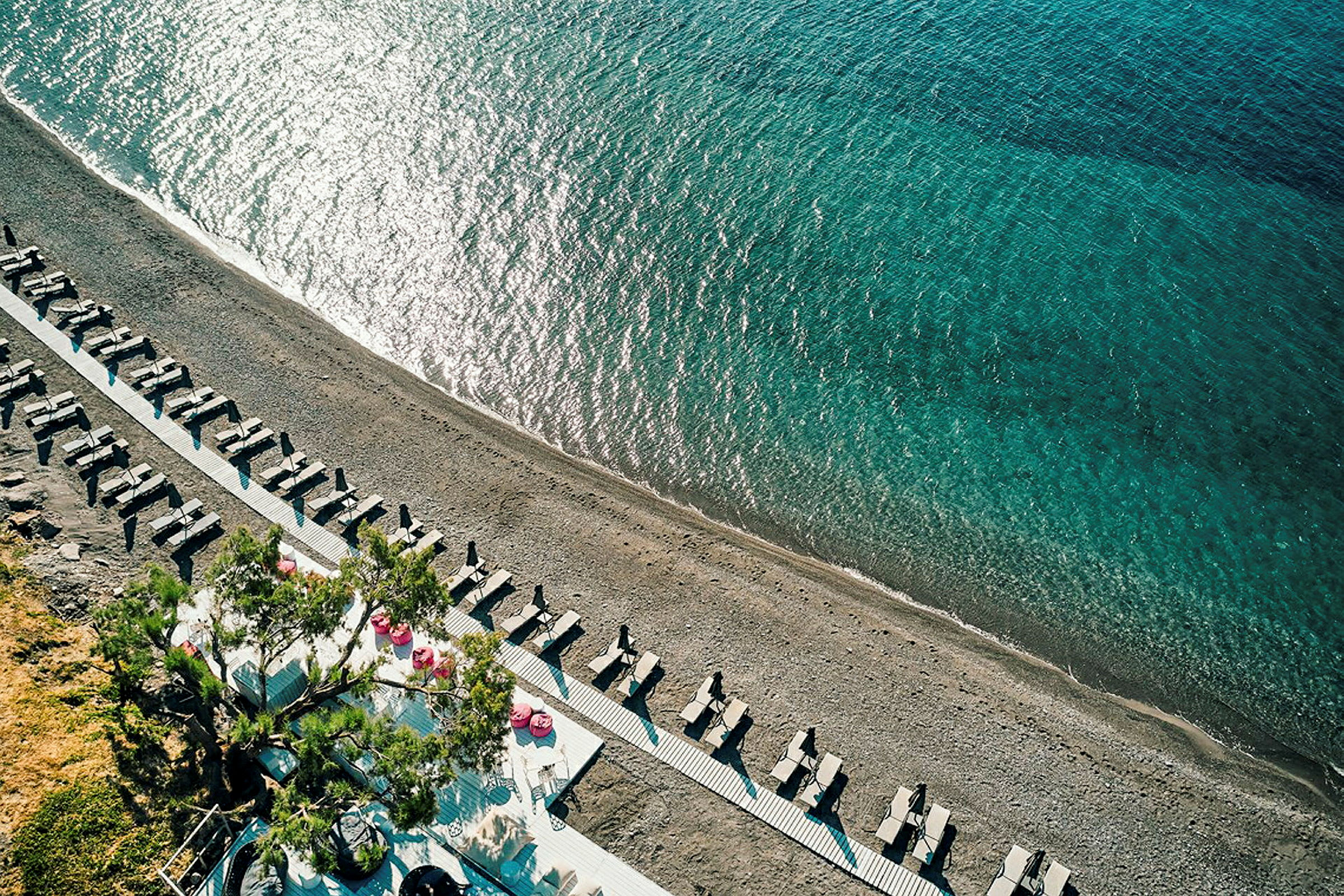 Flyfoto av en strand med solsenger og parasoller samt klart blått hav. (AI-generert tekst)