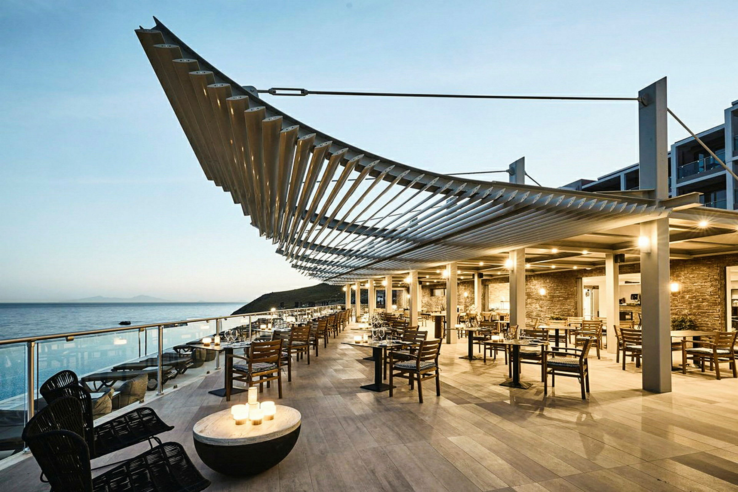 Restaurant med sitteplasser utendørs ved sjøen under en moderne pergola. (AI-generert tekst)