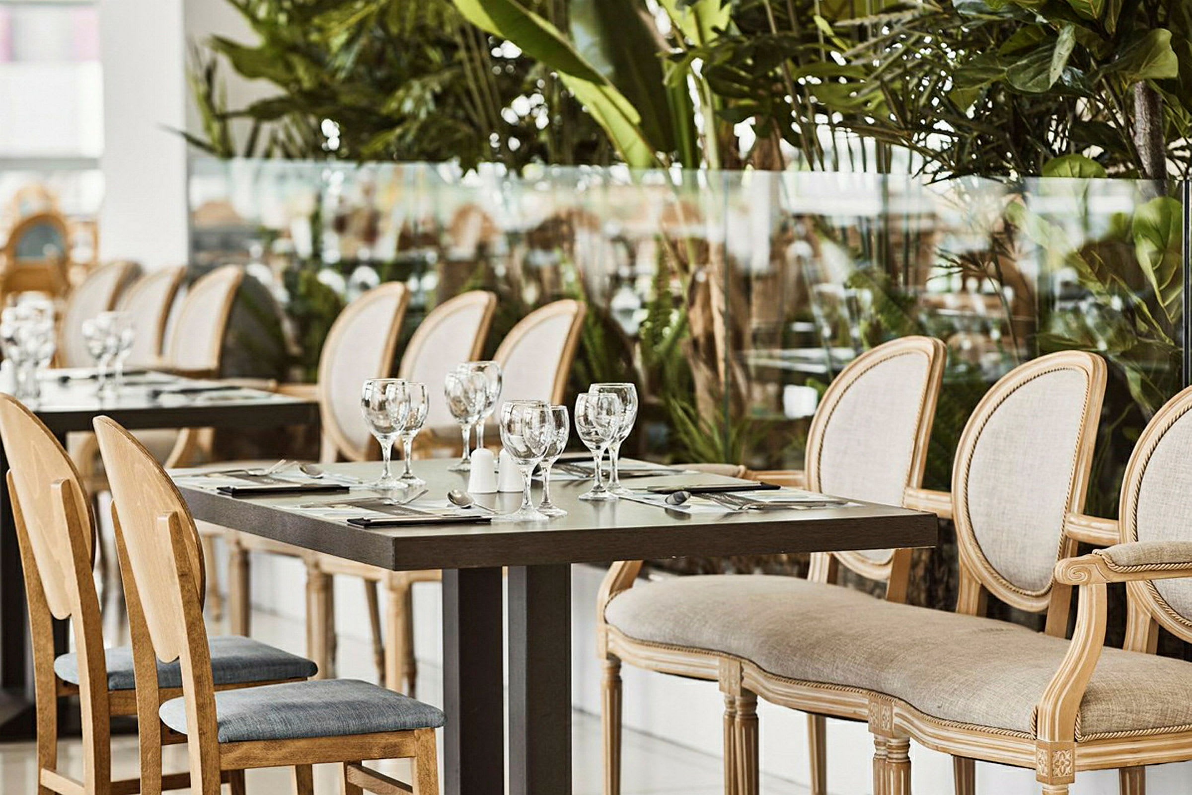 Et sett med spisebord og stoler i en restaurant omgitt av grøntområder. (AI-generert tekst)
