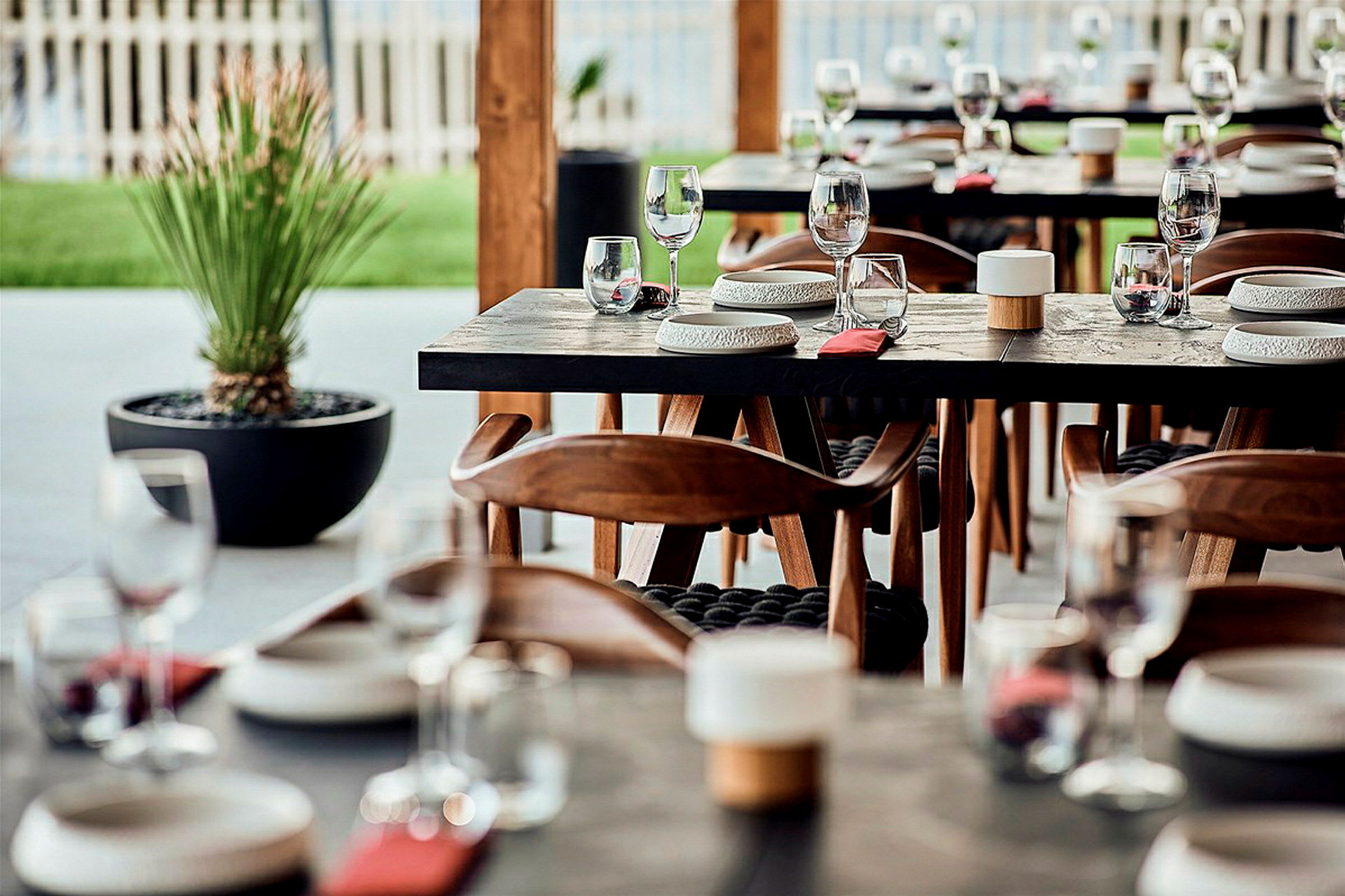 Et dekket bord med glass og tallerkener i en restaurant med trestoler og en plante i bakgrunnen. (AI-generert tekst)