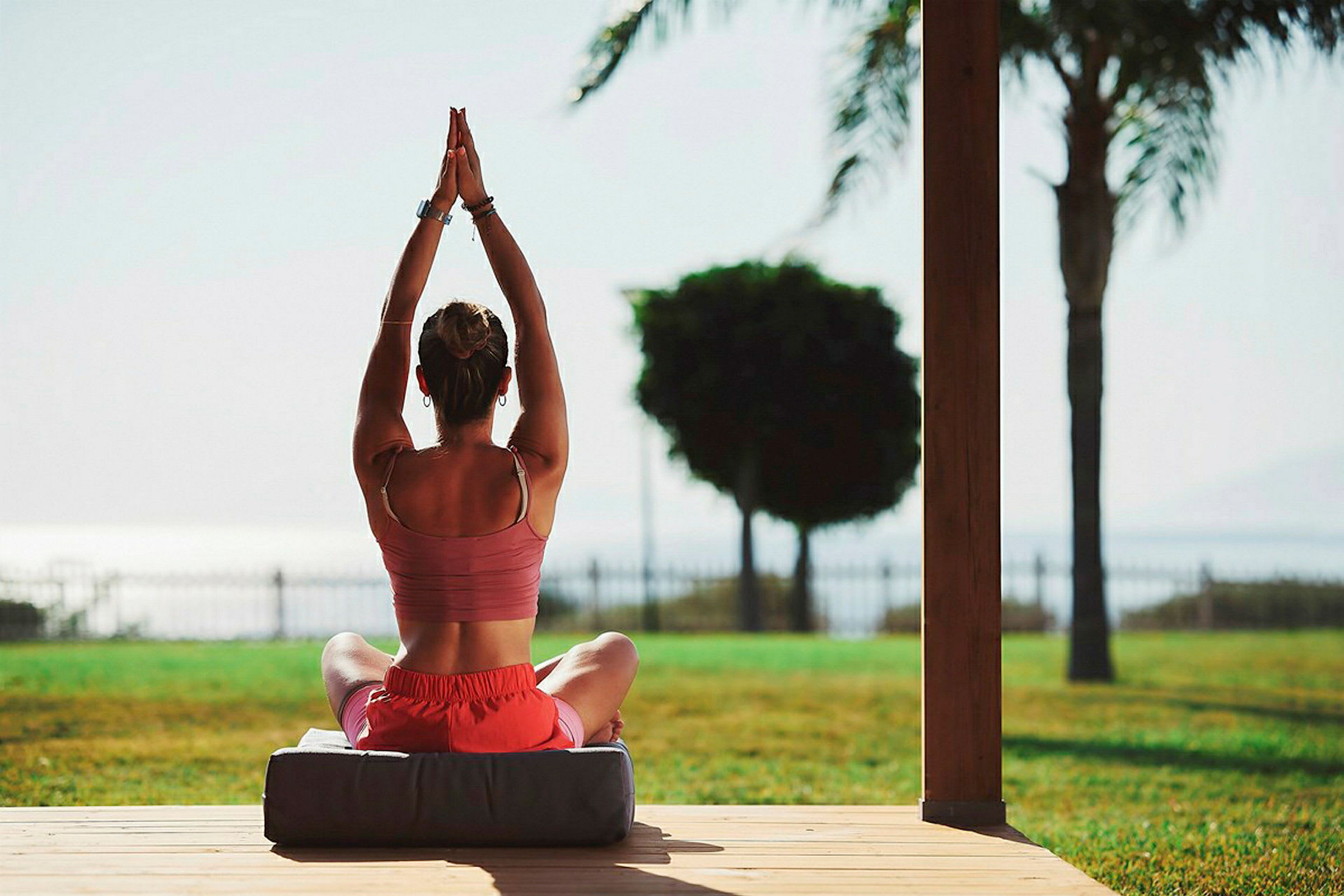 En person utfører yoga med hendene hevet i en sittende posisjon utendørs. (AI-generert tekst)