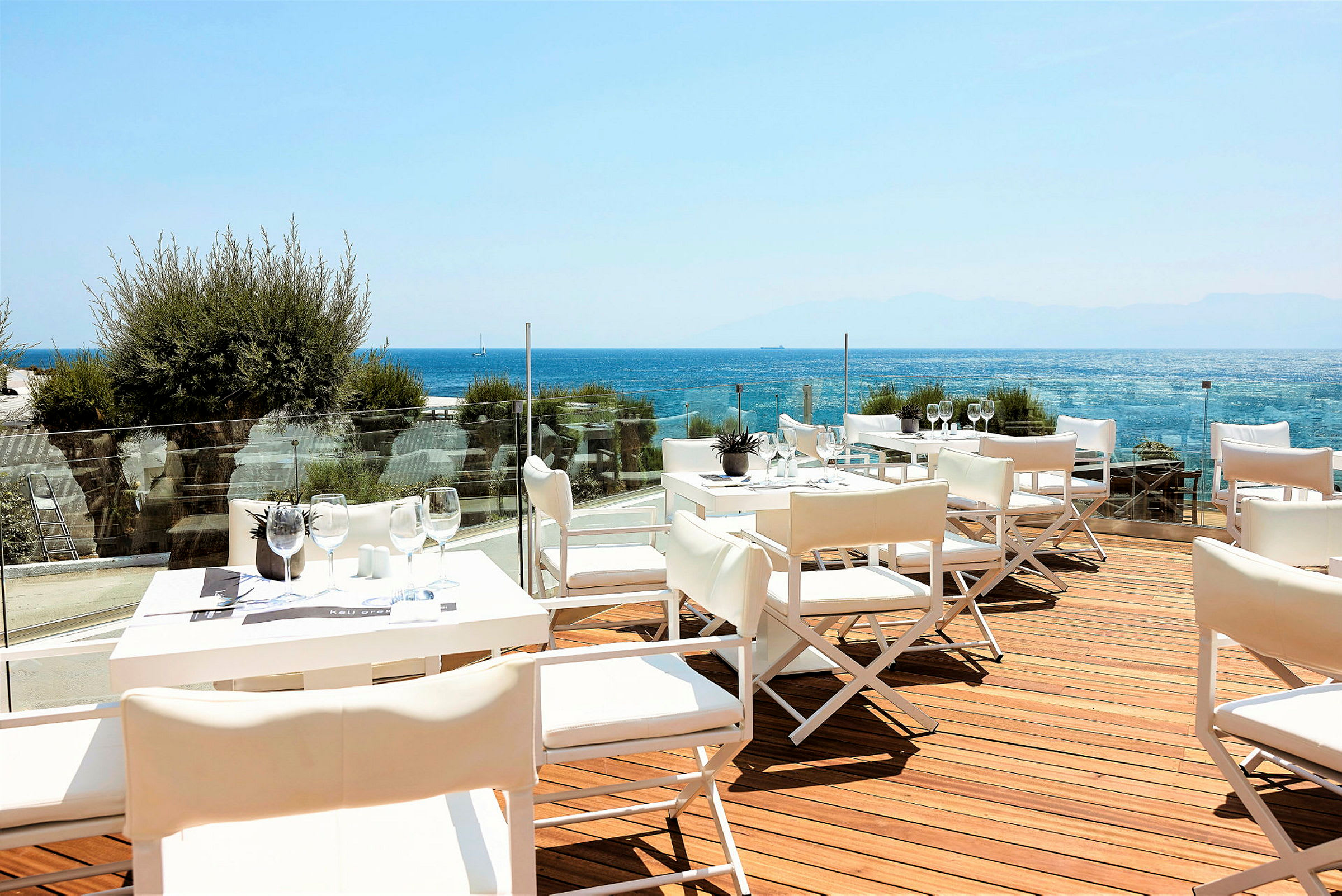 En terrasse med hvite bord og stoler, utsikt over havet. (AI-generert tekst)