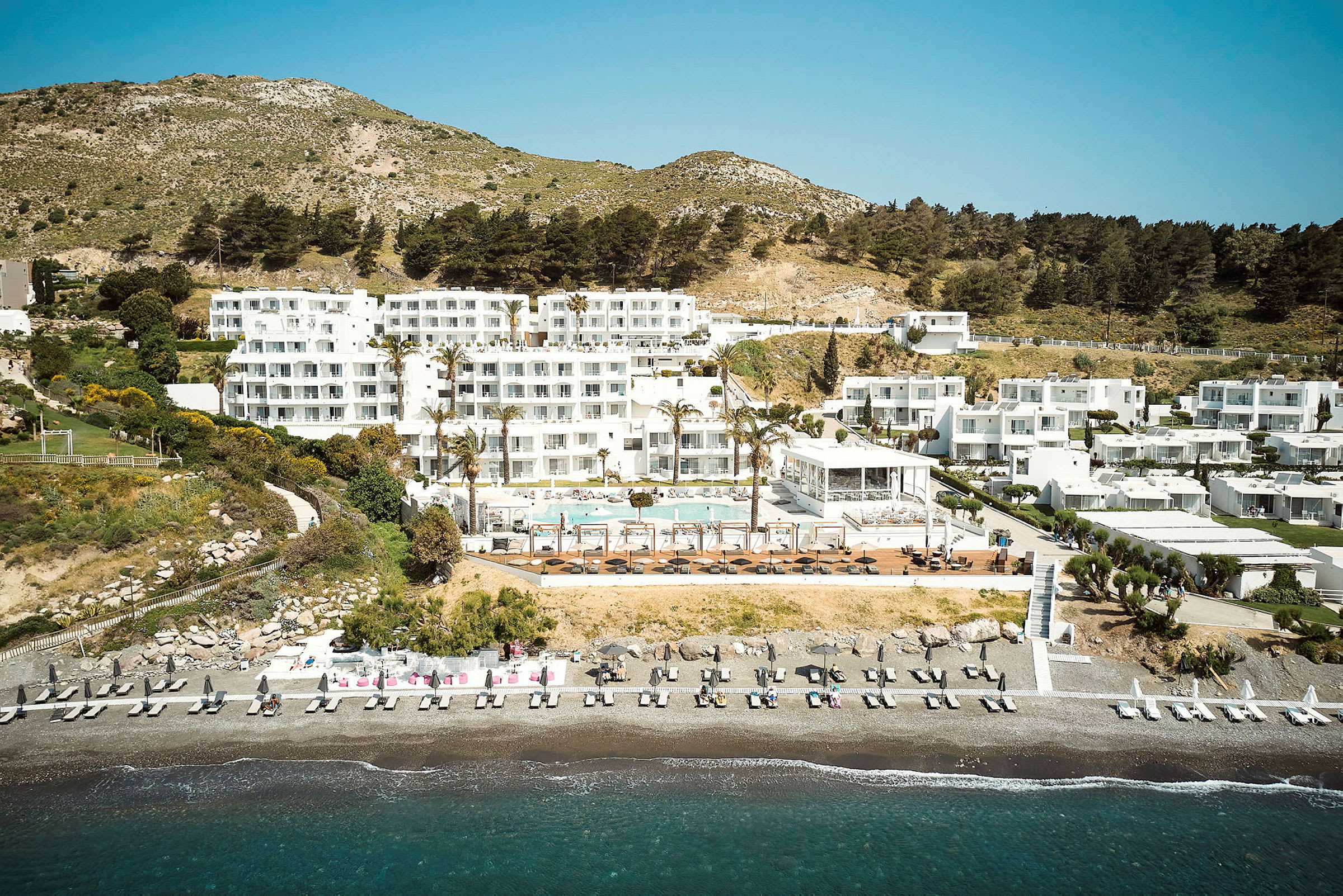 Hotellkompleks ved stranden med bassengområde og omkringliggende grøntområder. (AI-generert tekst)