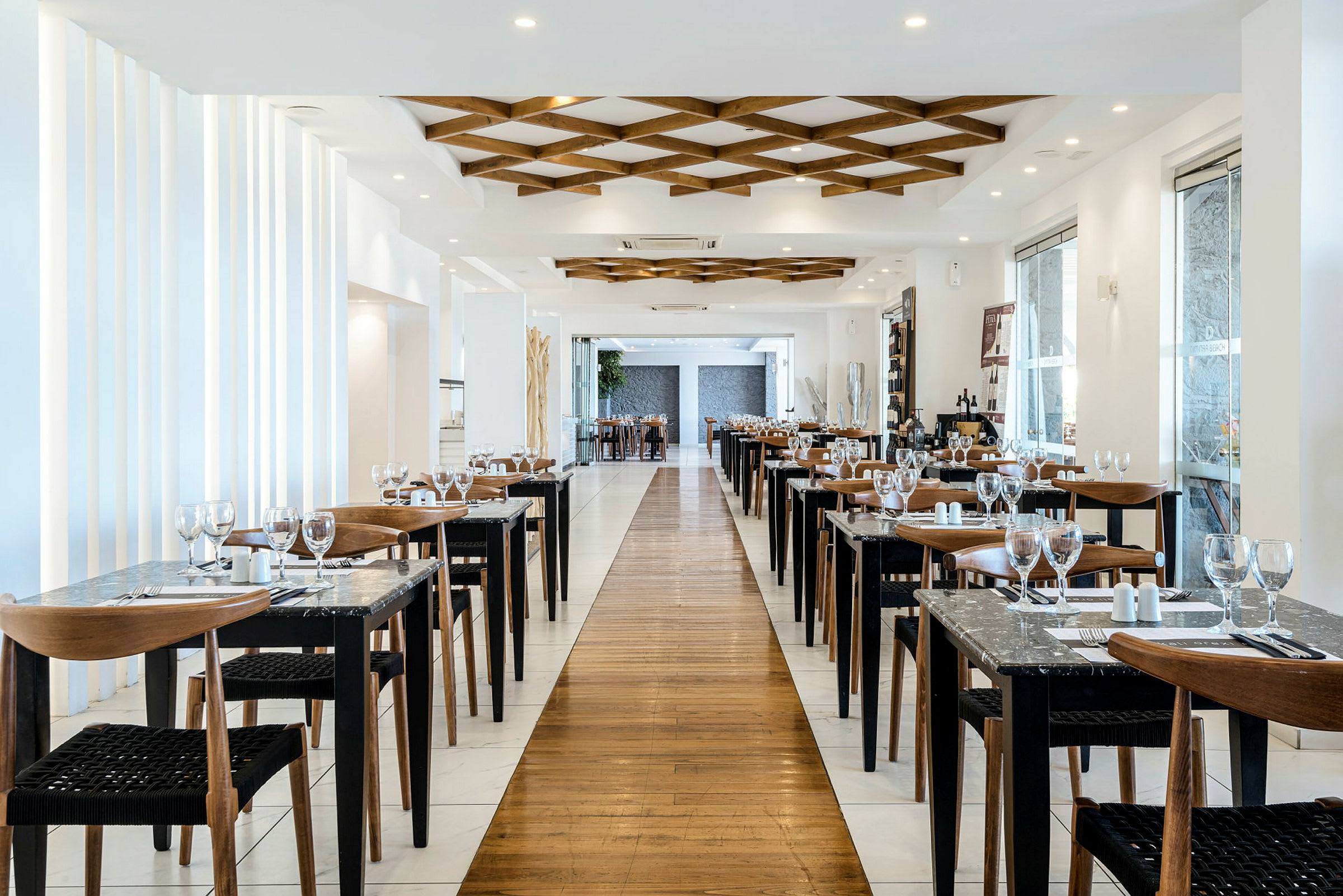 En elegant restaurant med oppstilte bord og stoler langs begge sider av en gangvei, dekorert med moderne interiør. (AI-generert tekst)