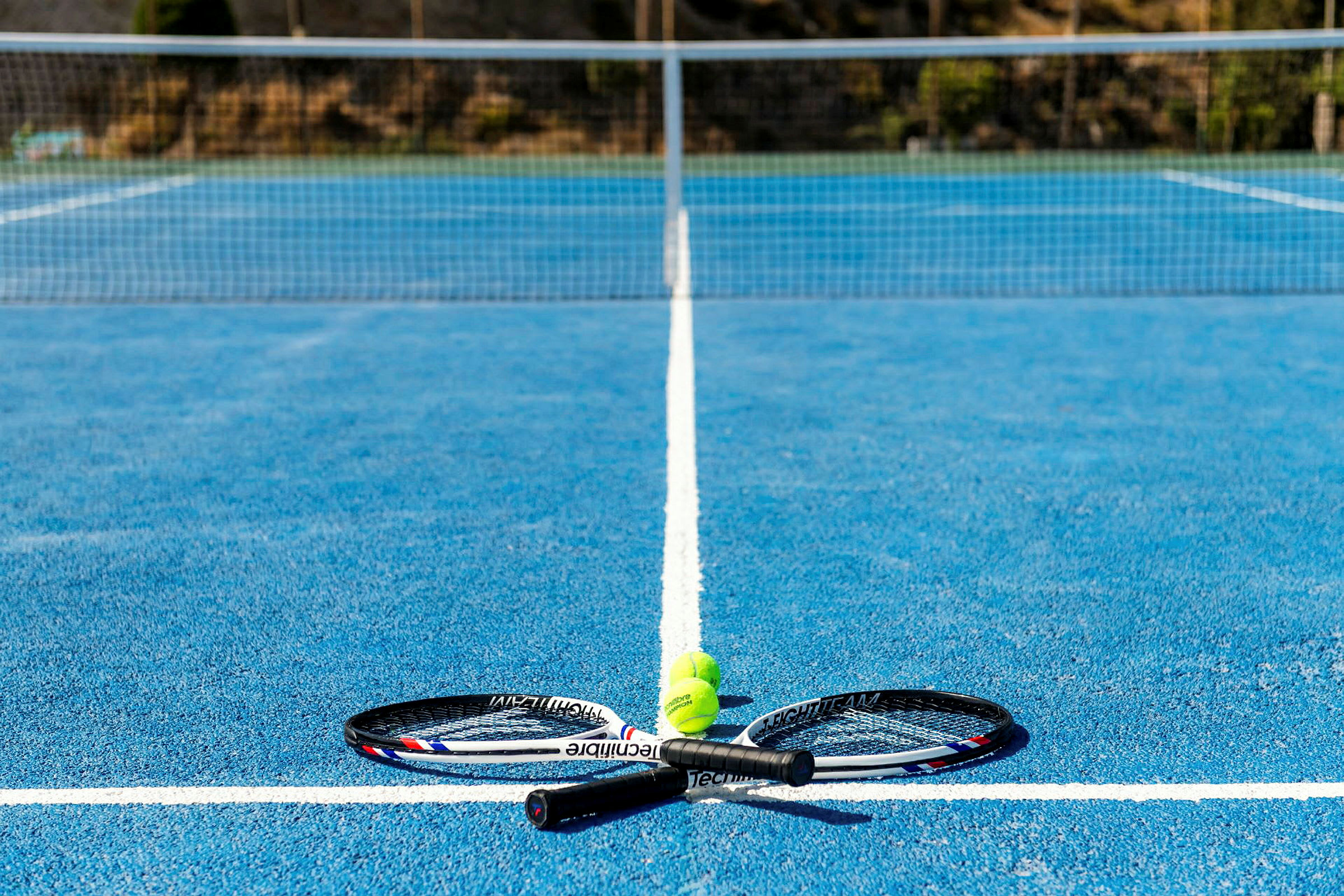 To tennisracketer og tre tennisballer på en blå tennisbane. (AI-generert tekst)