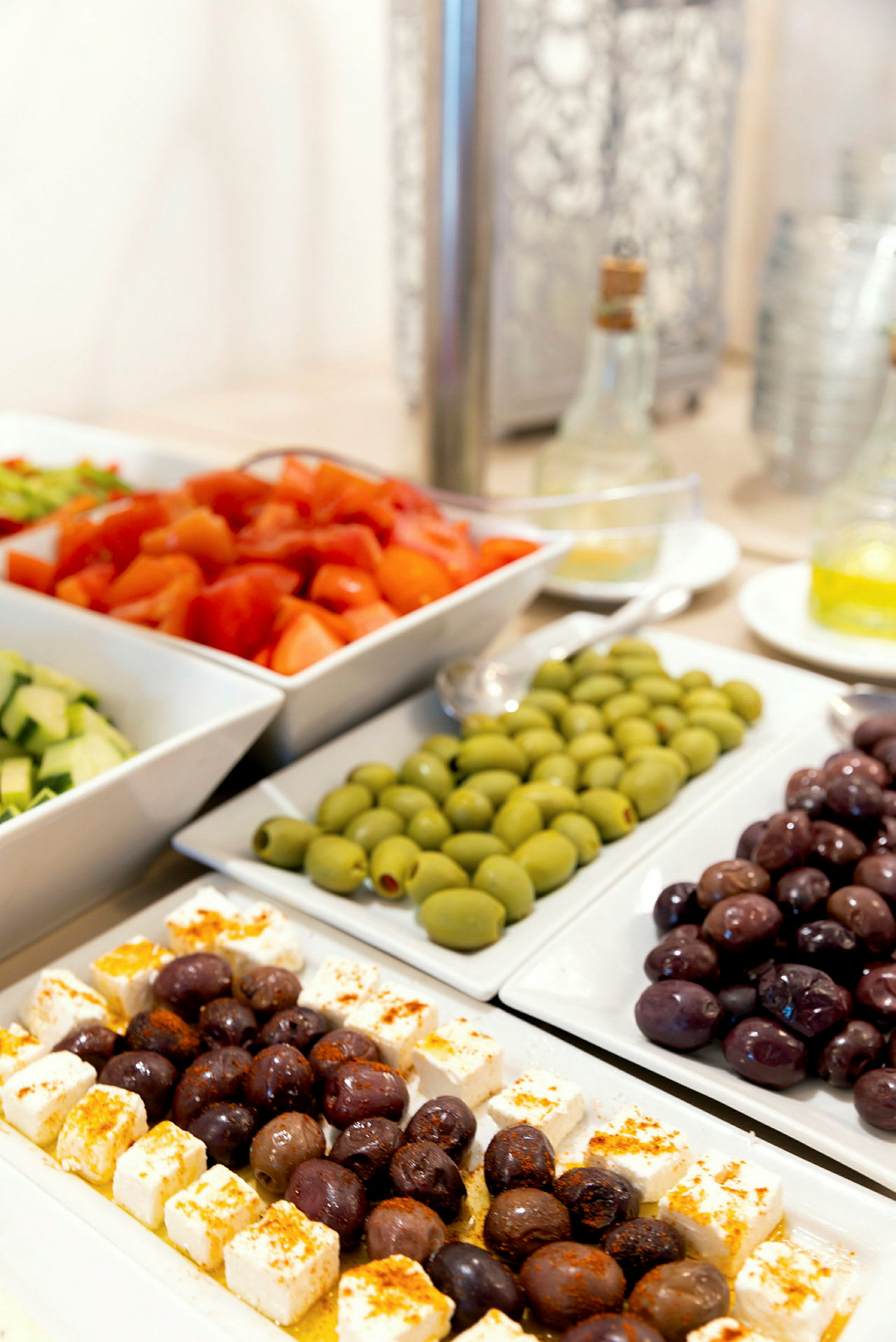 Flere serveringsfat med salatingredienser som oliven, fetaost og tomater. (AI-generert tekst)