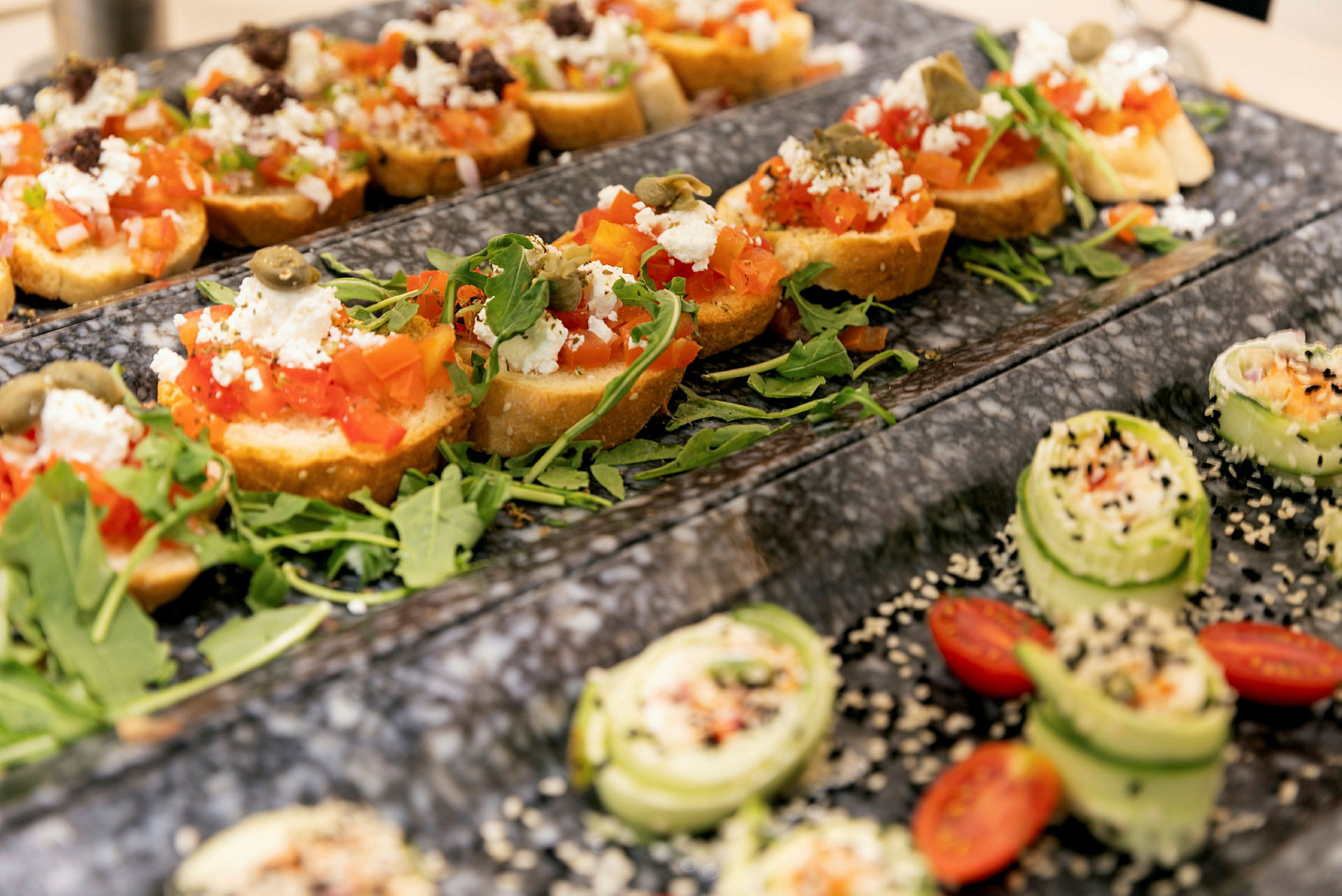 Anretting av bruschetta med tomat, fetaost og ruccola samt små agurksnitter med sesamfrø og cherrytomater. (AI-generert tekst)