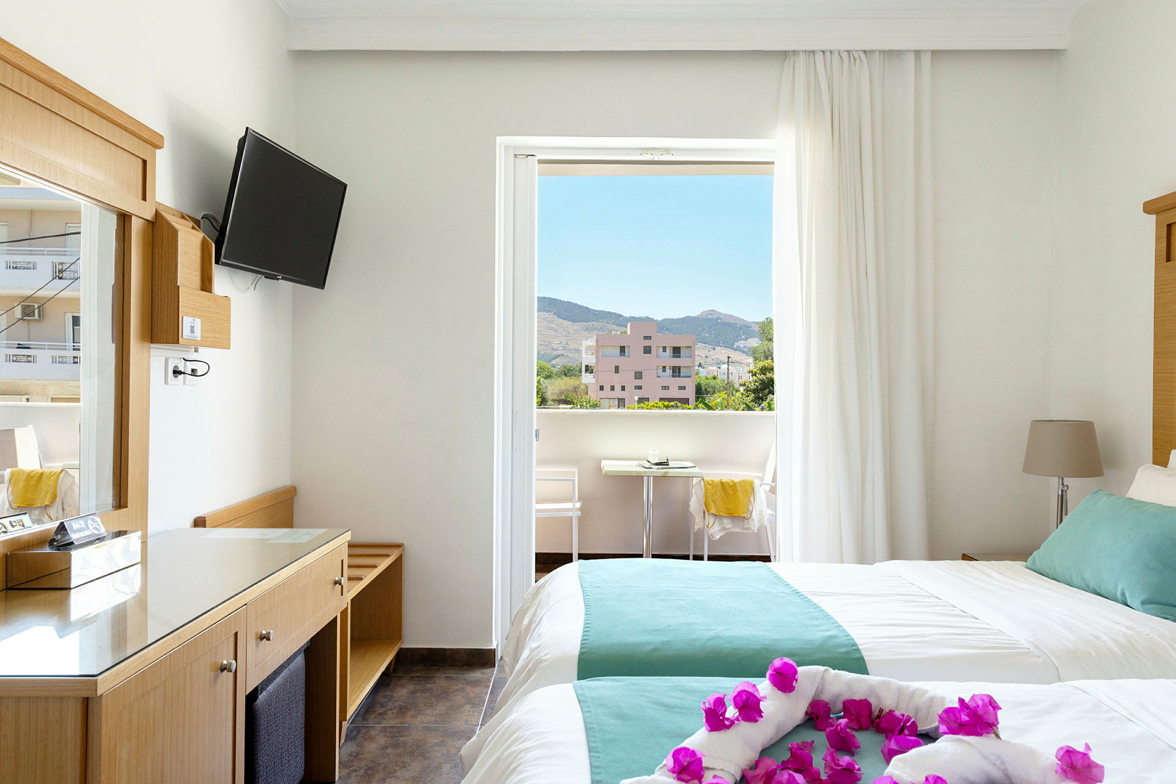 Hotellrom med to senger og balkong. Utsikt over omkringliggende bygninger og fjell. (AI-generert tekst)