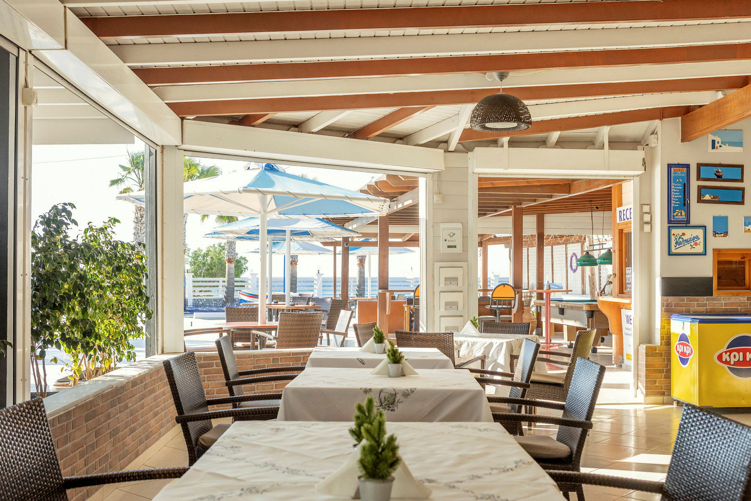 Restaurant med bord og stoler, utendørsområde med parasoller synlig i bakgrunnen. (AI-generert tekst)