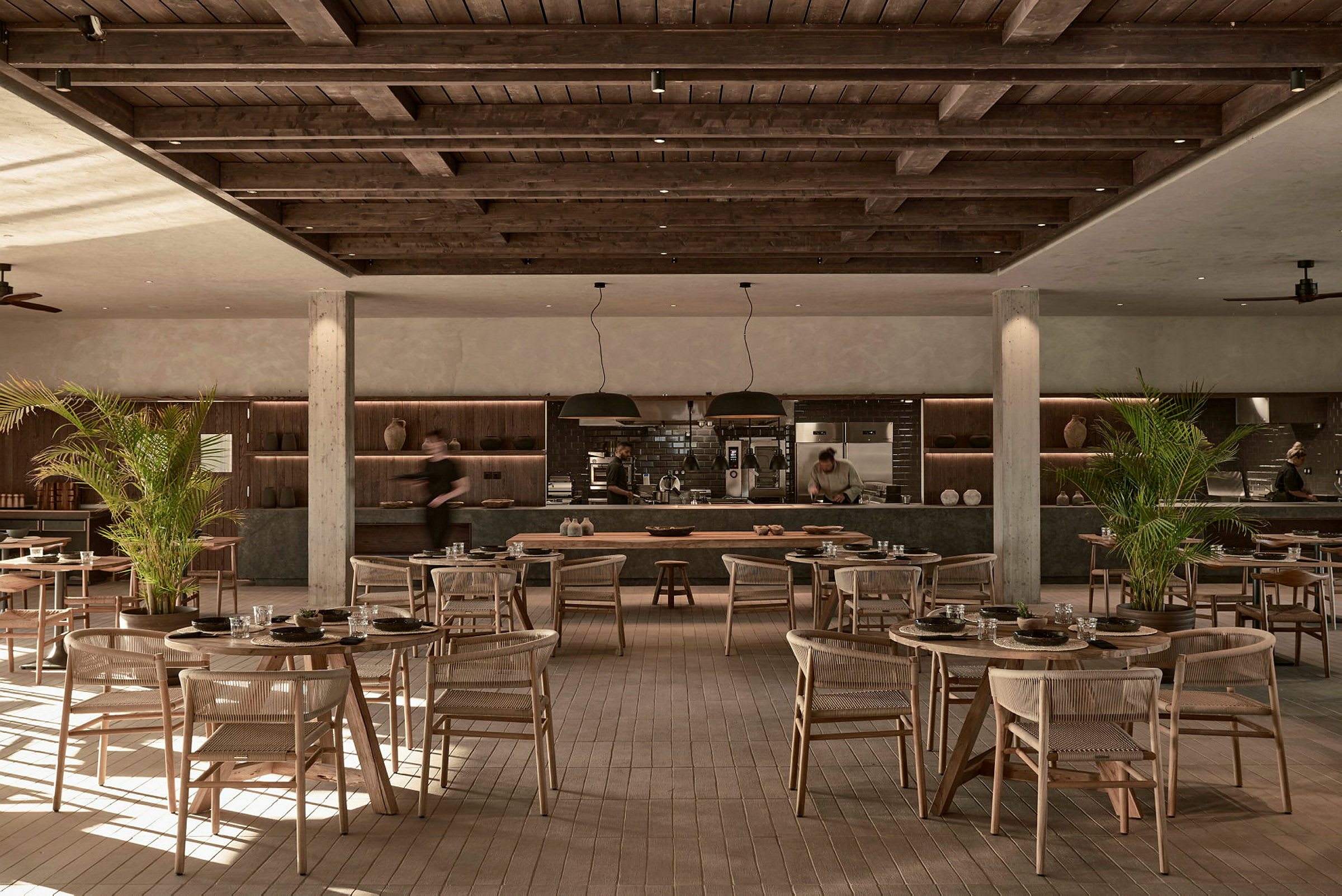 Restaurant med treinteriør og bord spredt over gulvet, med åpen kjøkkenområde i bakgrunnen. (AI-generert tekst)