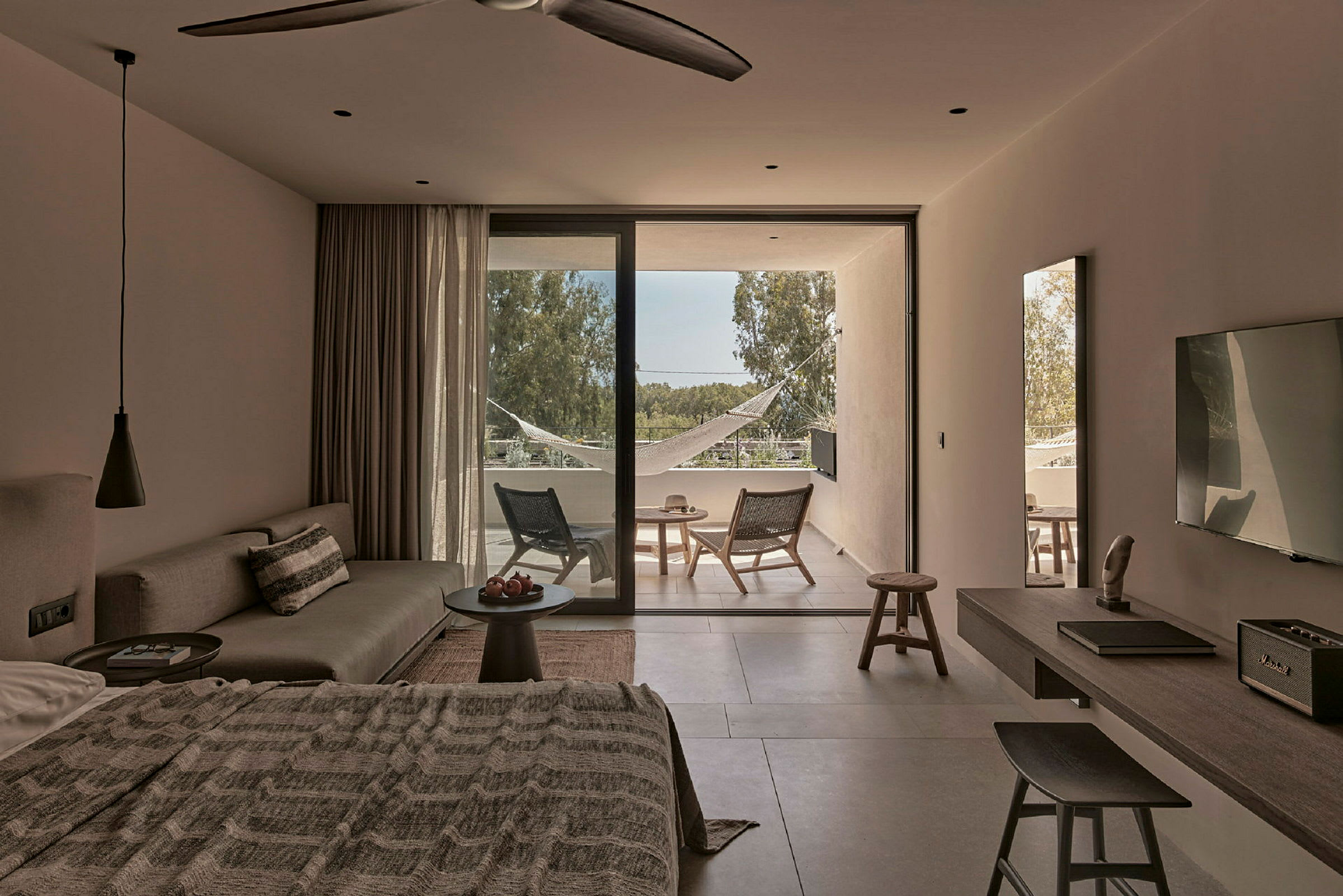 Et moderne hotellrom med seng, sofa, bord og terrasse med stoler og hengekøye. (AI-generert tekst)