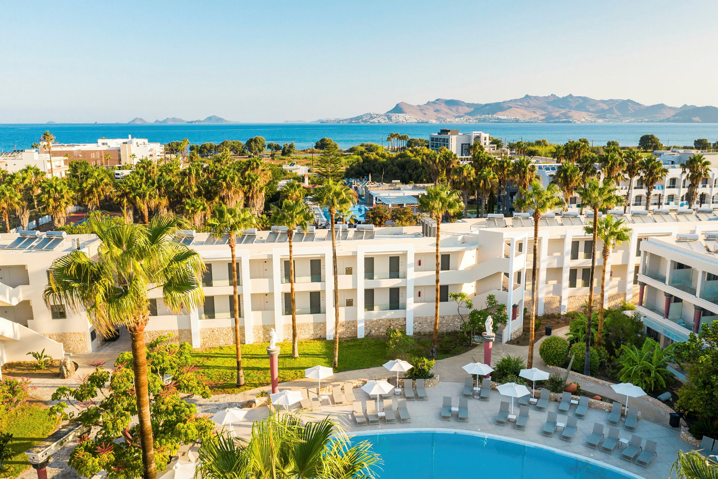 Hotellets utside med bassengområde og utsikt mot havet og fjellene. (AI-generert tekst)