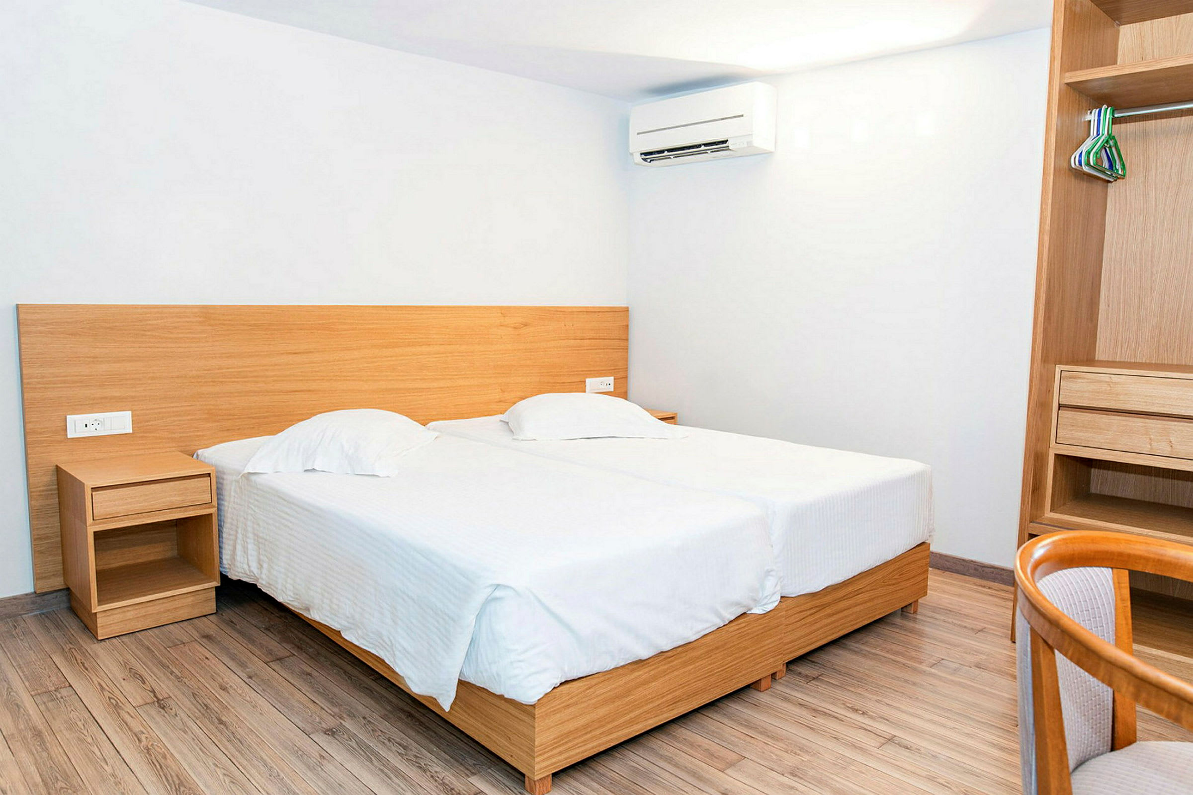 Interiør av et hotellrom med to enkeltsenger og et åpent skap. (AI-generert tekst)