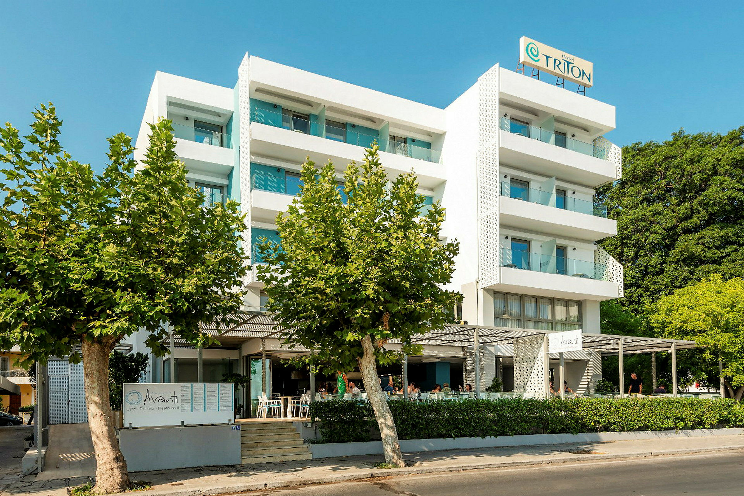 Flereetasjes hotell med hvite fasader, balkonger og restaurant foran bygningen. (AI-generert tekst)