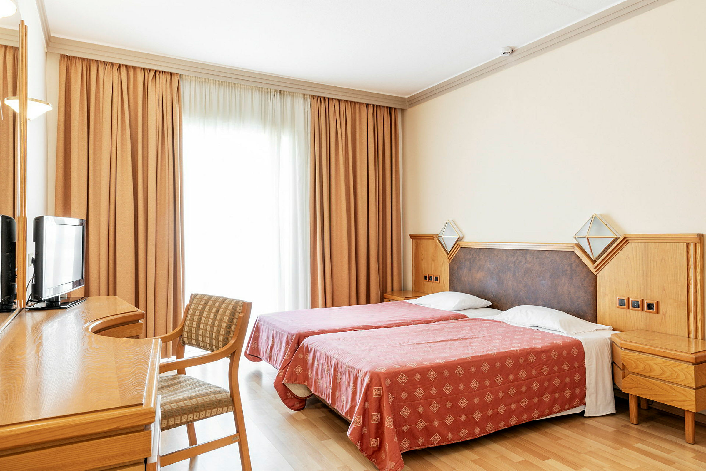 Hotellrom med to enkeltsenger, skrivebord, stol og TV. (AI-generert tekst)