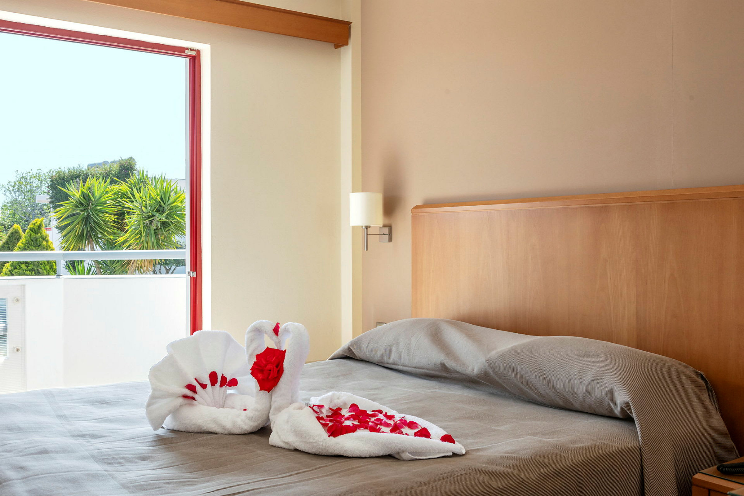 Bilde av en seng i et hotellrom med håndkler brettet som svaner dekorert med røde roseblader. (AI-generert tekst)