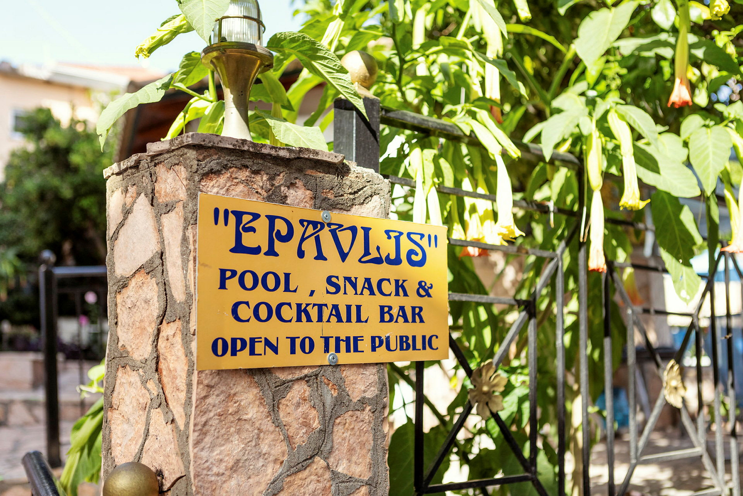 Skilt på en steinsøyle med teksten 'EPAVLIS Pool, Snack & Cocktail Bar Open to the public'. (AI-generert tekst)