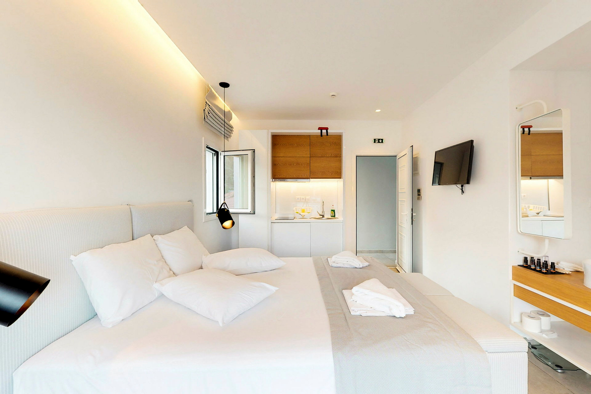 Et moderne hotellrom med en dobbeltseng, en veggmontert TV og en liten kjøkkenkrok. (AI-generert tekst)