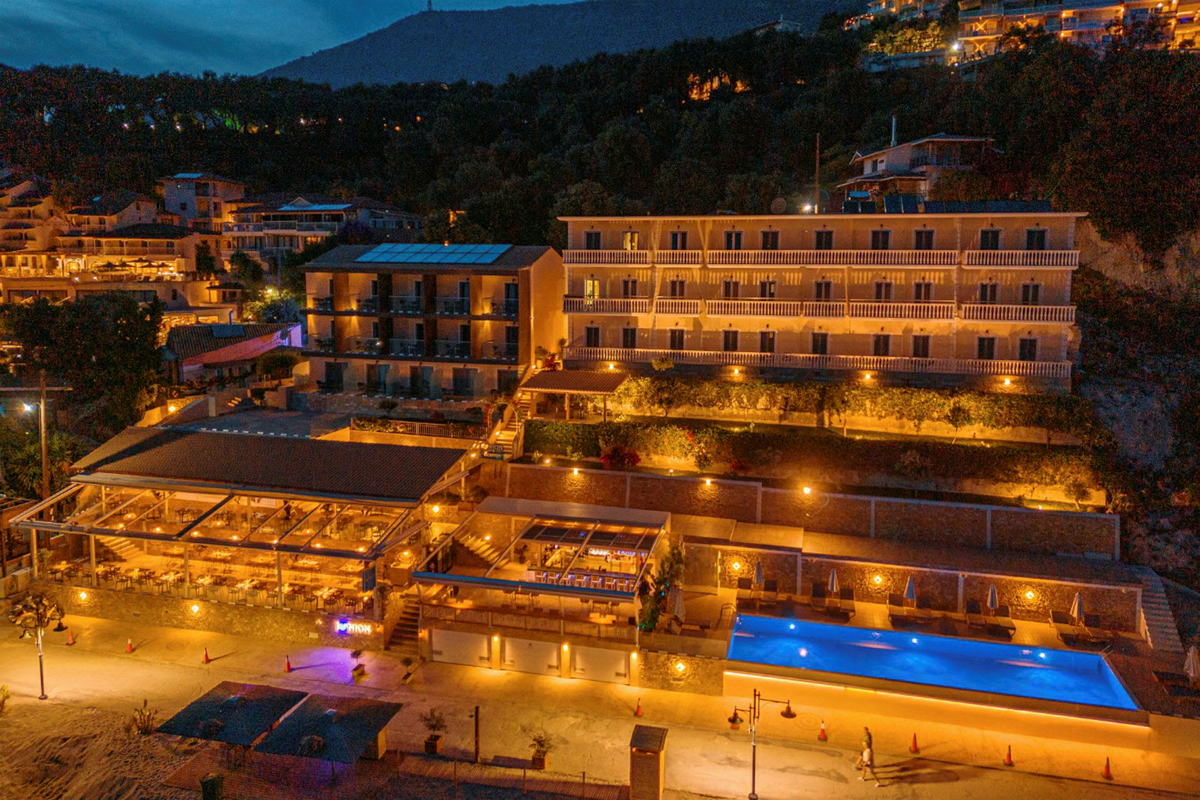 Hotellbygning med basseng og restaurant opplyst om kvelden. (AI-generert tekst)