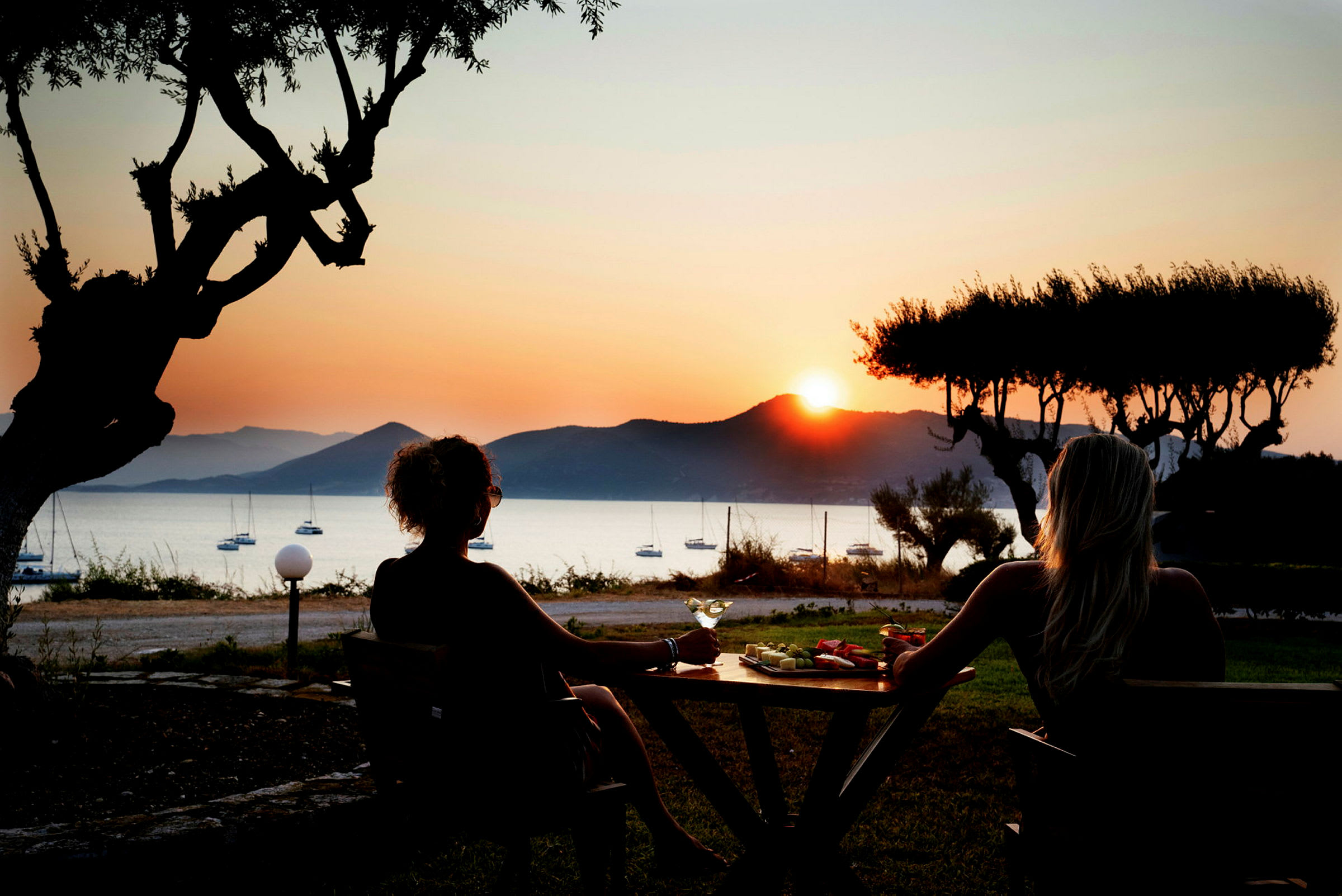 To personer sitter ved et bord og nyter utsikten over havet ved solnedgang. (AI-generert tekst)