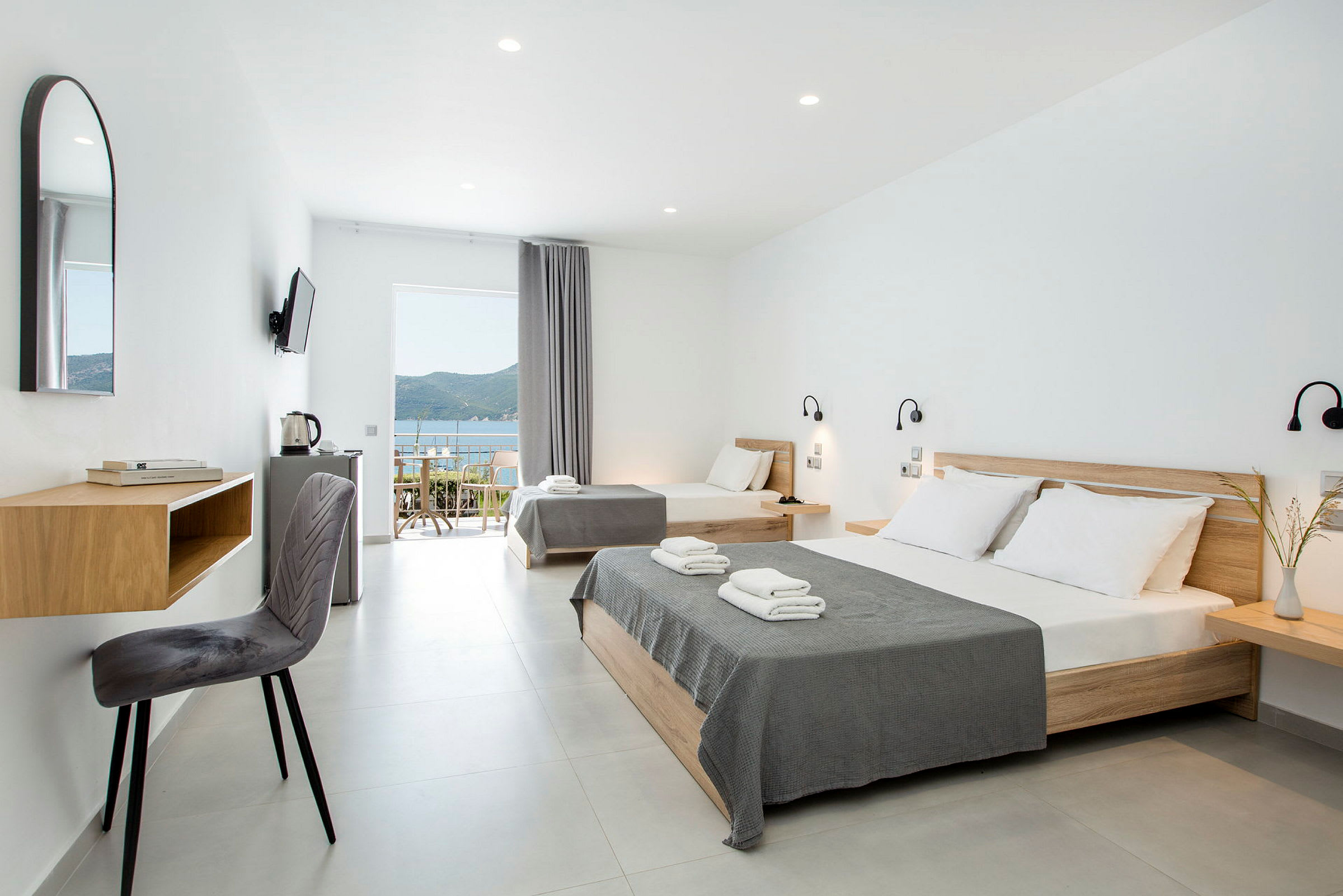 Moderne hotellrom med lyse vegger, dobbeltseng og enkeltseng samt havutsikt. (AI-generert tekst)