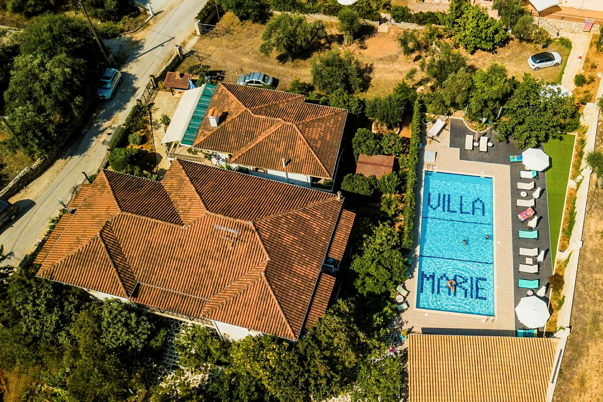 Luftfoto av en villa med oransje tegltak og et blått basseng på eiendommen. Basseng har teksten 'Villa Marie'. (AI-generert tekst)