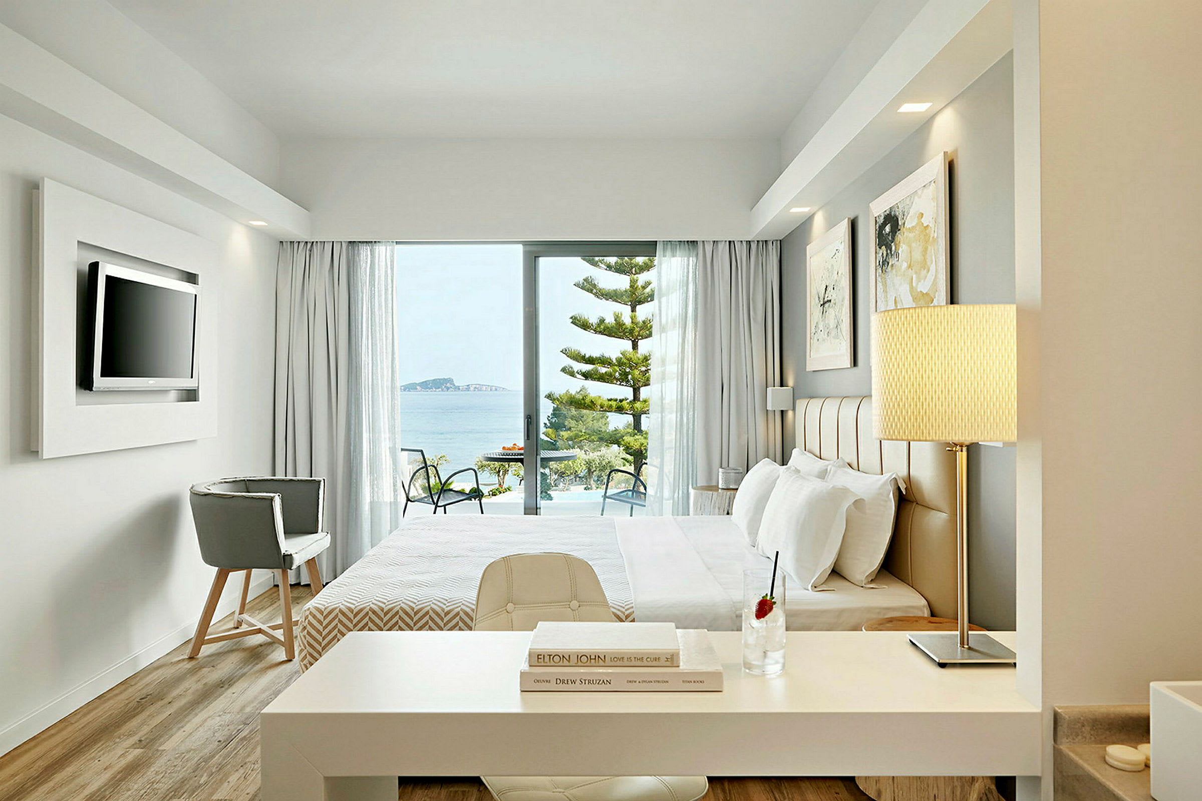 Et hotellrom med moderne innredning og vinduer som vender ut mot en balkong med utsikt over havet. (AI-generert tekst)