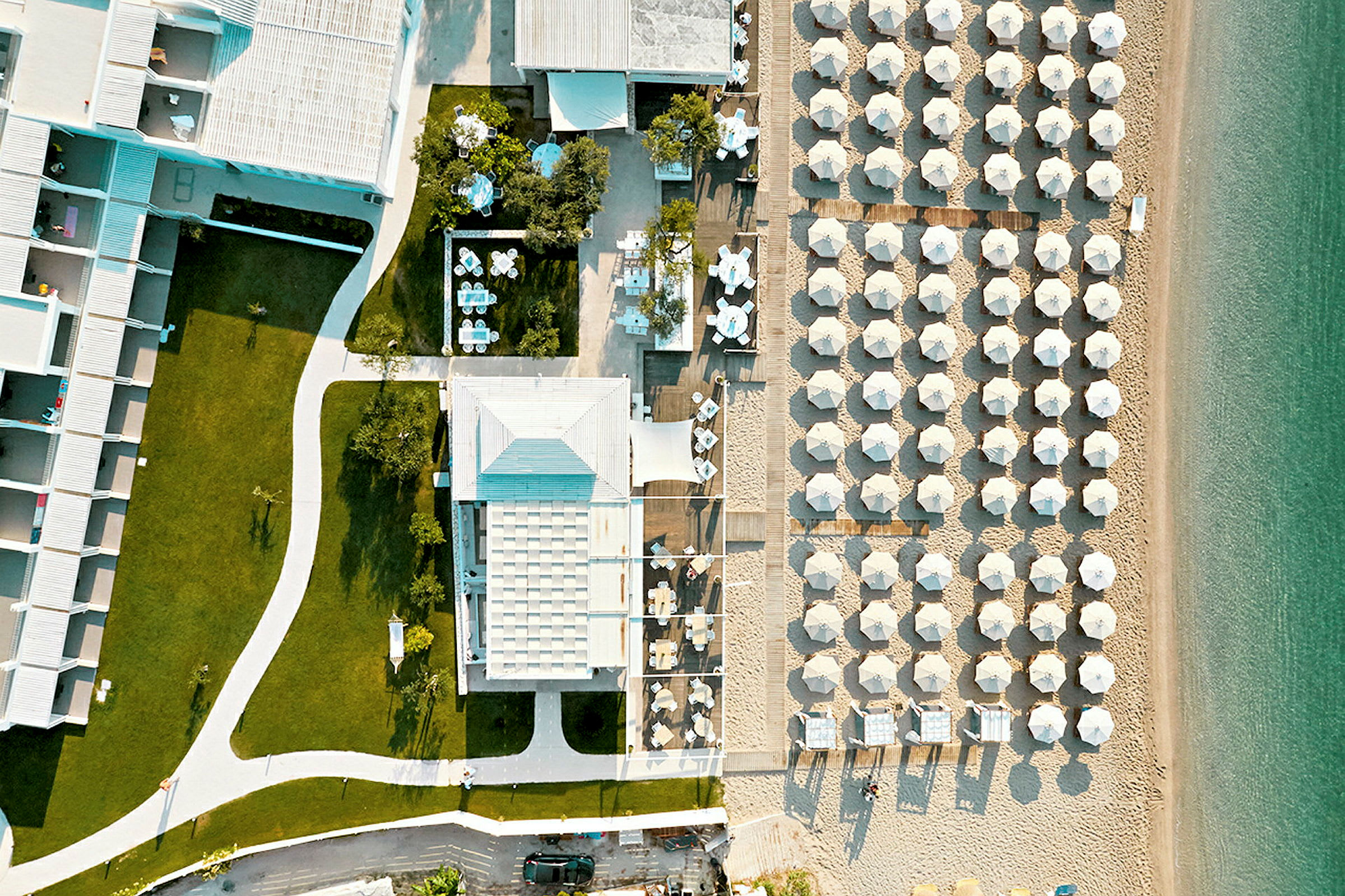 Flyfoto av hotellbygning med plener og strand med parasoller. (AI-generert tekst)