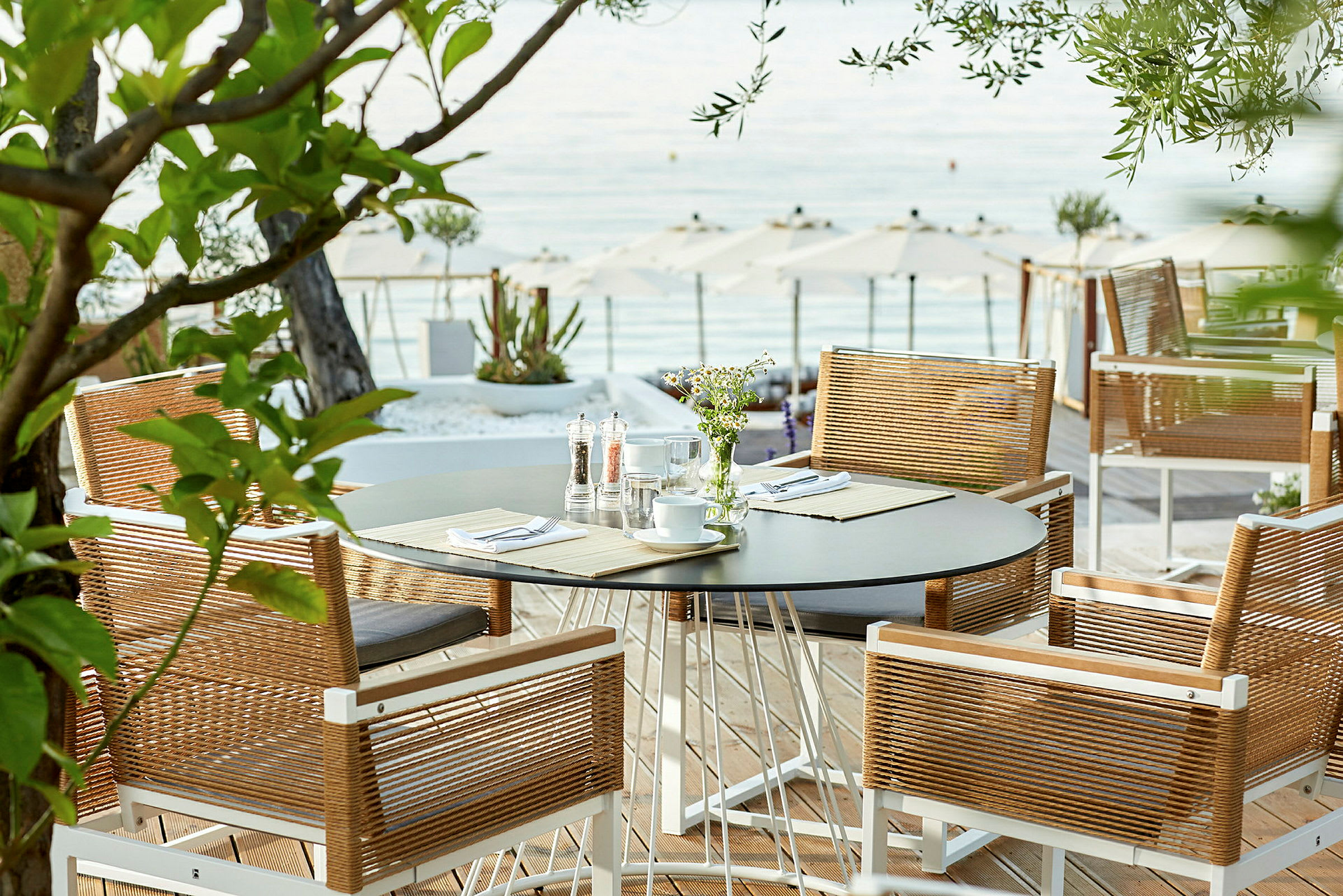 Utsikt mot et bord med stoler på en terrasse nær havet. (AI-generert tekst)
