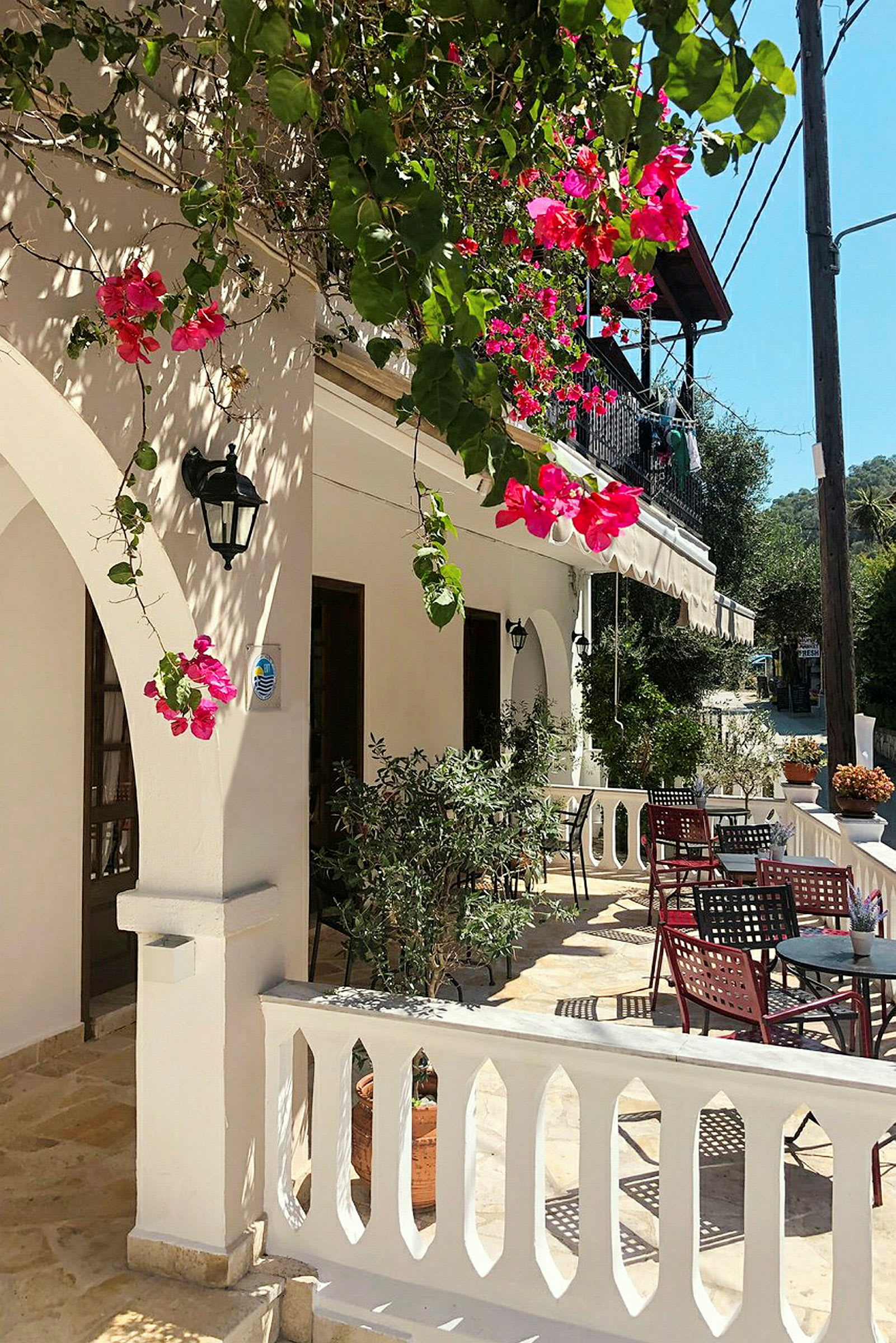 En solfylt uteplass med hvite balustrader og bord omgitt av blomstrende bougainvillea. (AI-generert tekst)