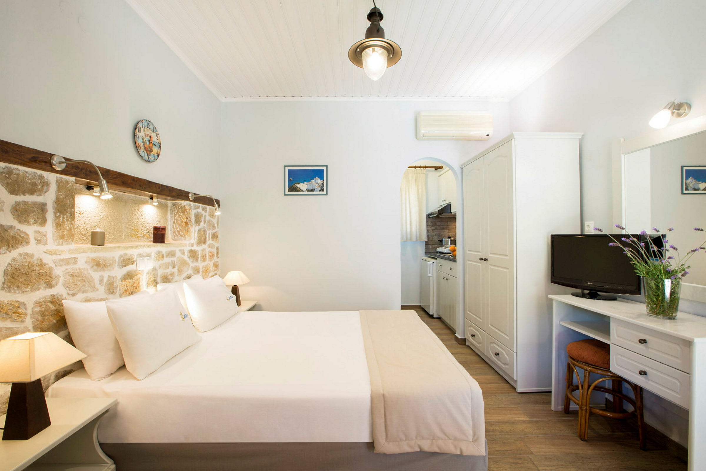 Hotellrom med dobbeltseng, murvegg og liten kjøkkenkrok. (AI-generert tekst)