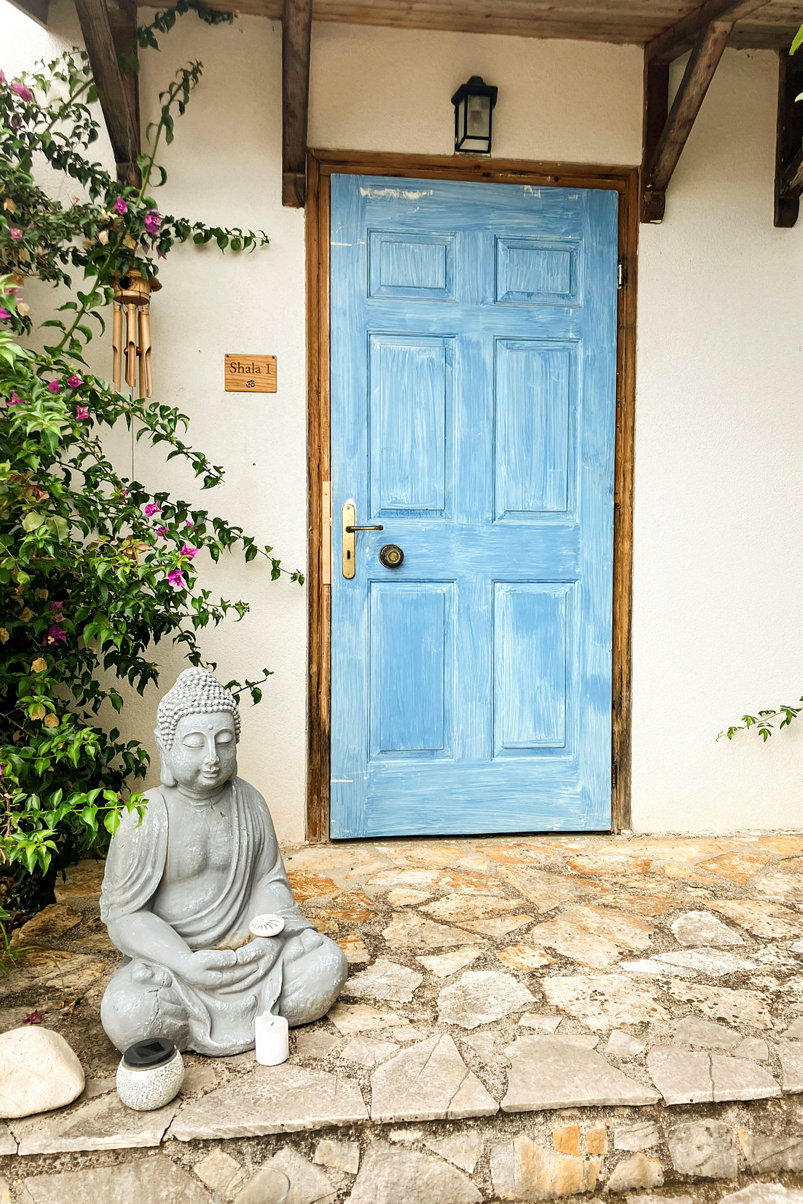 En blåmalt dør med en steinstatue av en sittende Buddha foran. (AI-generert tekst)