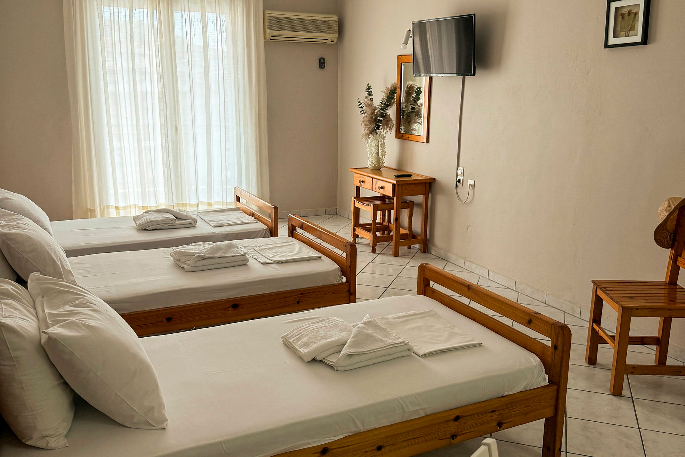 Tre enkeltsenger i et hotellrom med tremøbler, et skrivebord og en TV på veggen. (AI-generert tekst)