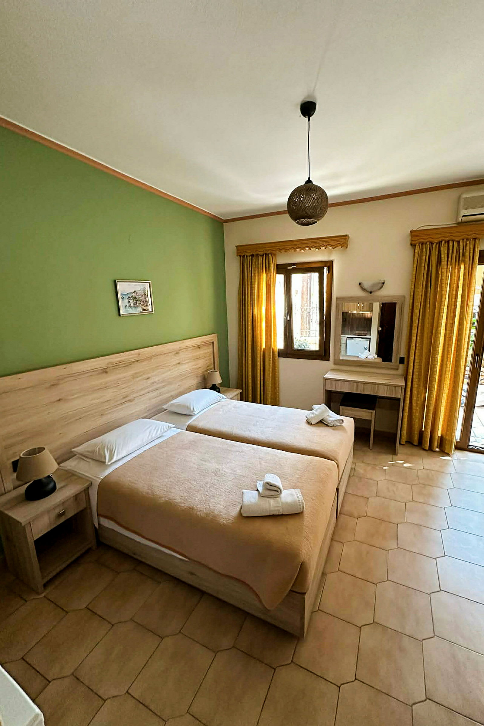 Hotellrom med to enkeltsenger, grønn vegg, beige sengetøy og møbler, samt vindu med gule gardiner. (AI-generert tekst)