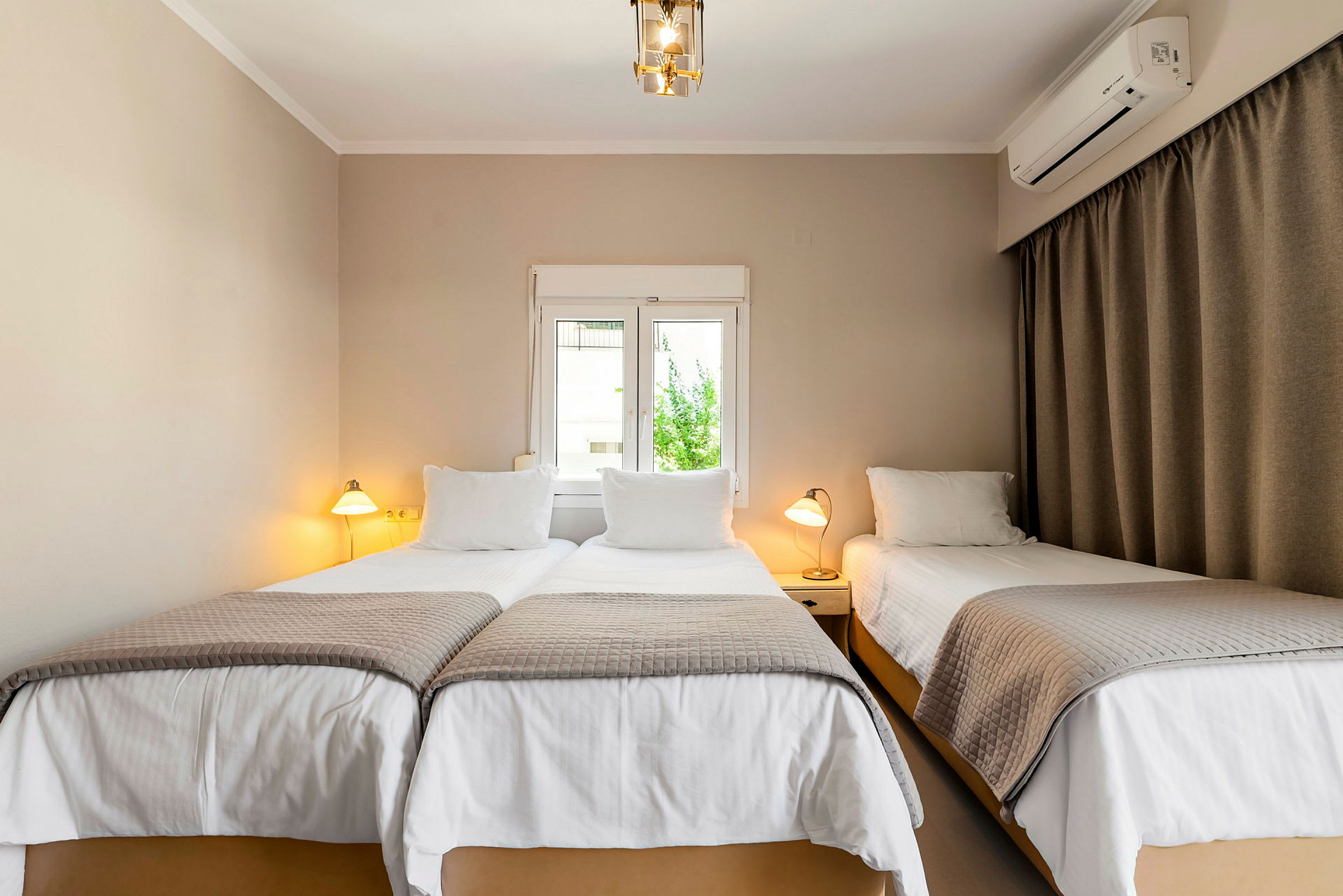 Et hotellrom med tre enkeltsenger, to sammen og en separat, alle med hvite laken og gråe sengetepper. (AI-generert tekst)