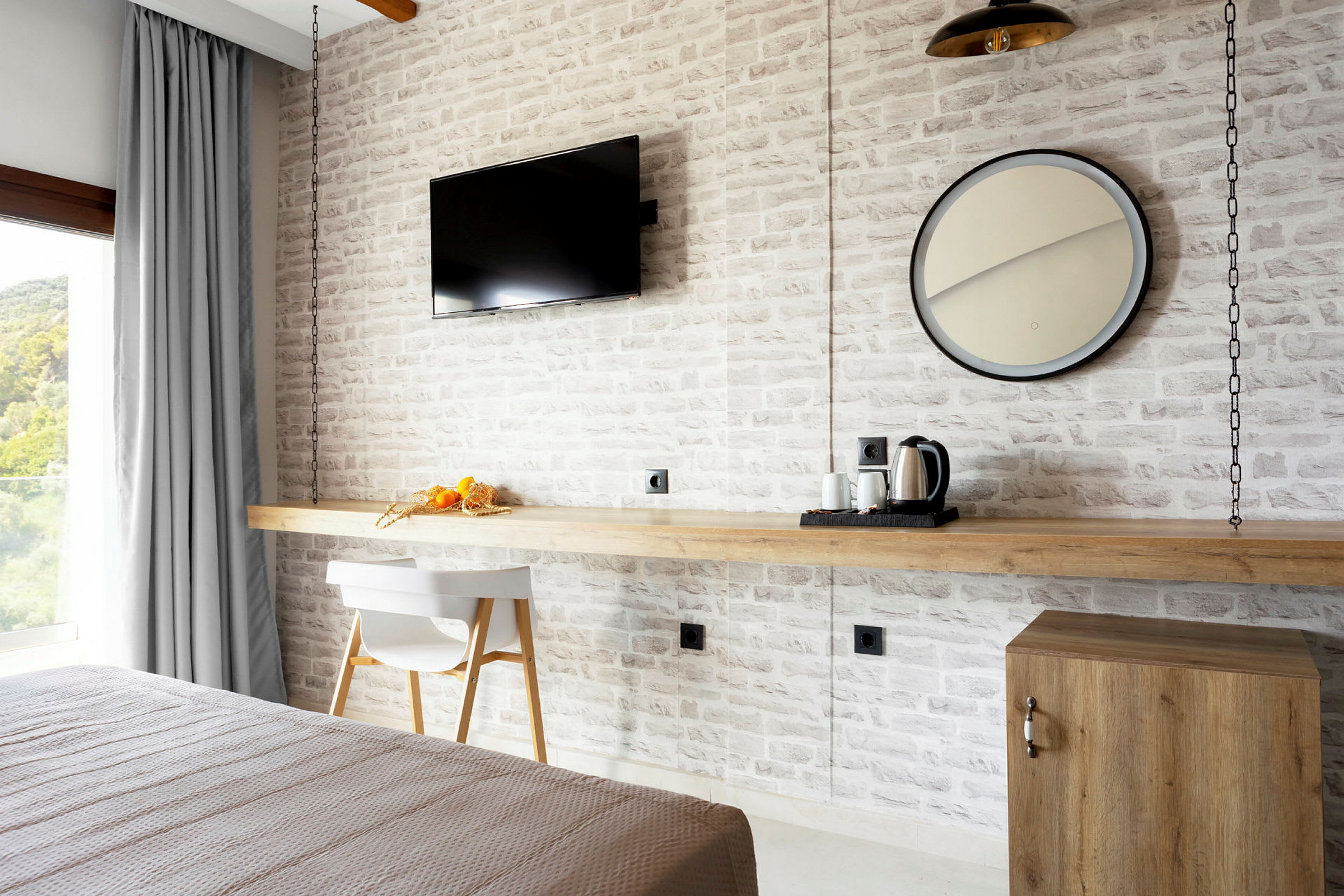 Et hotellrom med en hvit teglveg, en moderne TV, et rundt speil og bord med kaffetrakter. (AI-generert tekst)