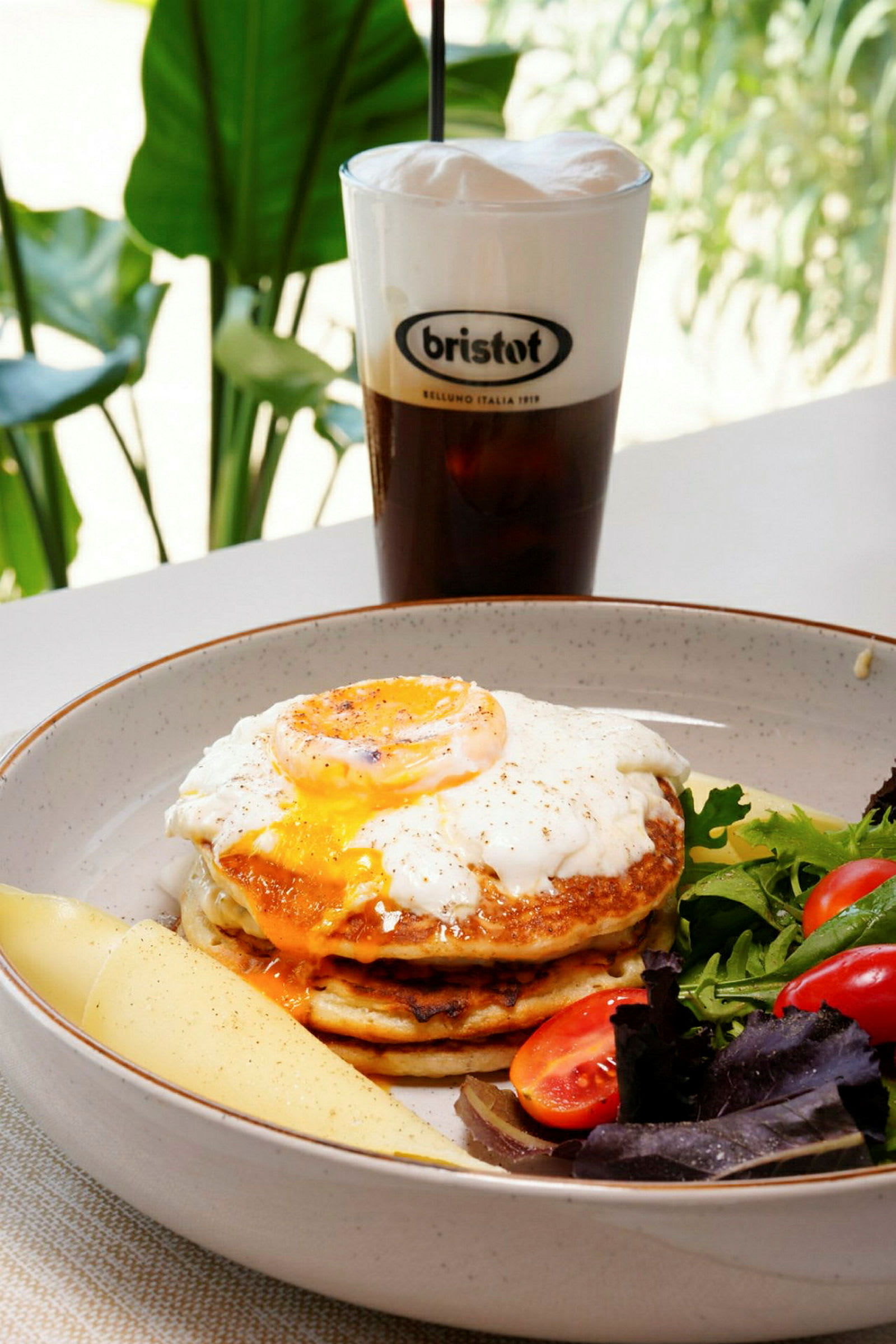 En tallerken med pannekaker, stekt egg på toppen, salat og en drikke i bakgrunnen. (AI-generert tekst)