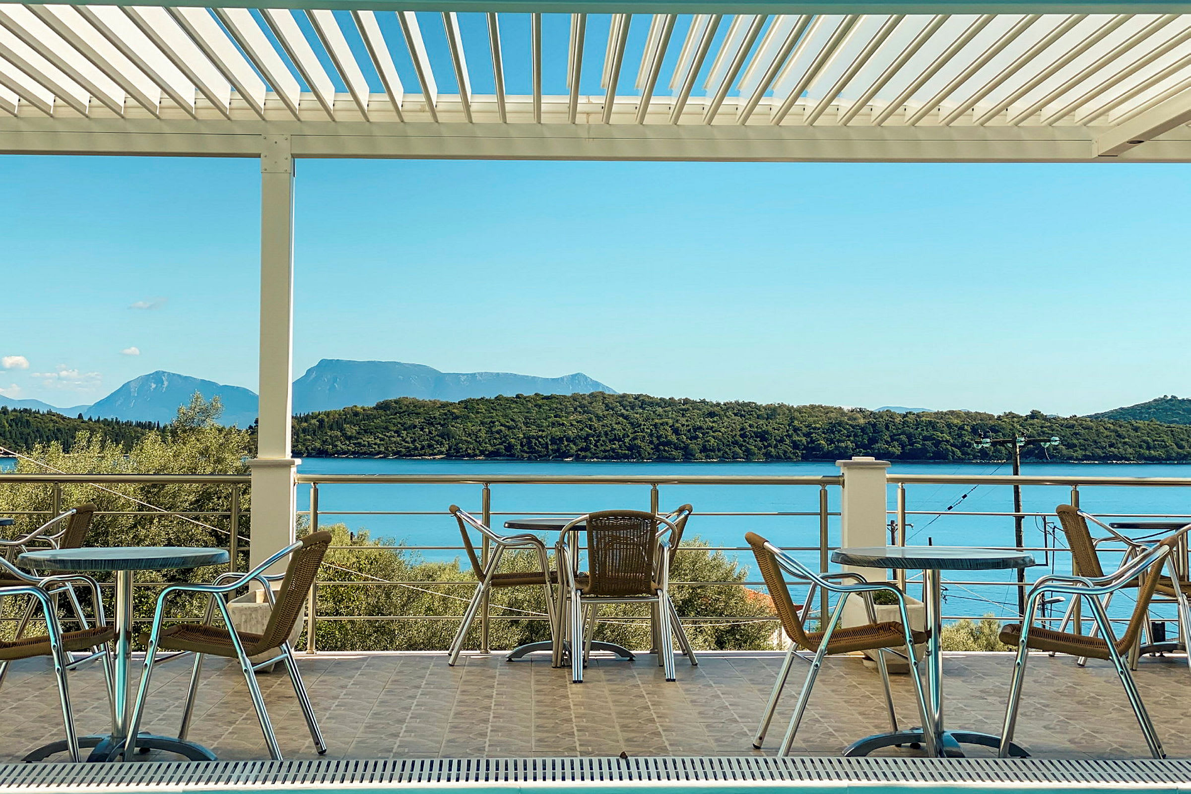 Utemøbler med bord og stoler på en terrasse med utsikt over havet og skogkledde åser. (AI-generert tekst)